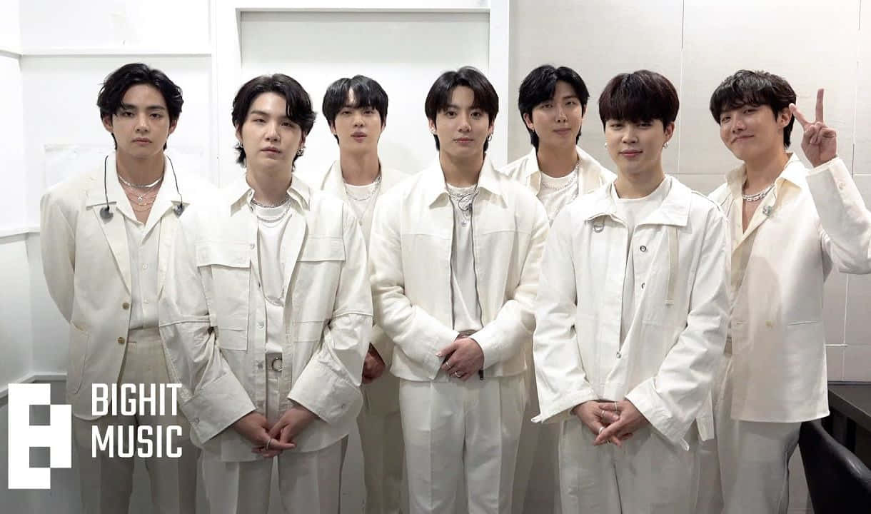 七位身穿白色服裝的K-pop偶像在帶有BIGHIT MUSIC標誌的攝影棚中擺姿勢。 — Bts 壁紙