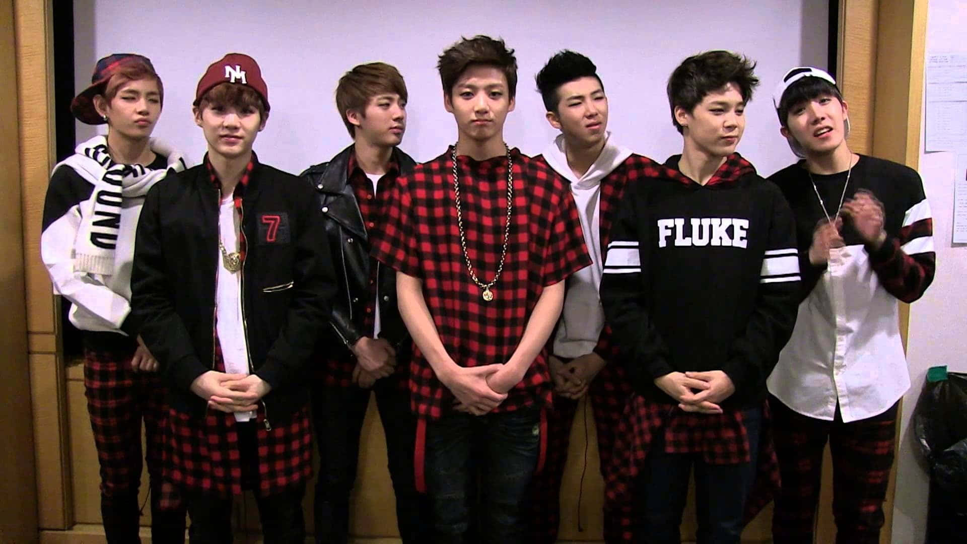七位身穿相配紅色格紋服飾的年輕男性K-pop偶像正在拍照。 — Bts 壁紙