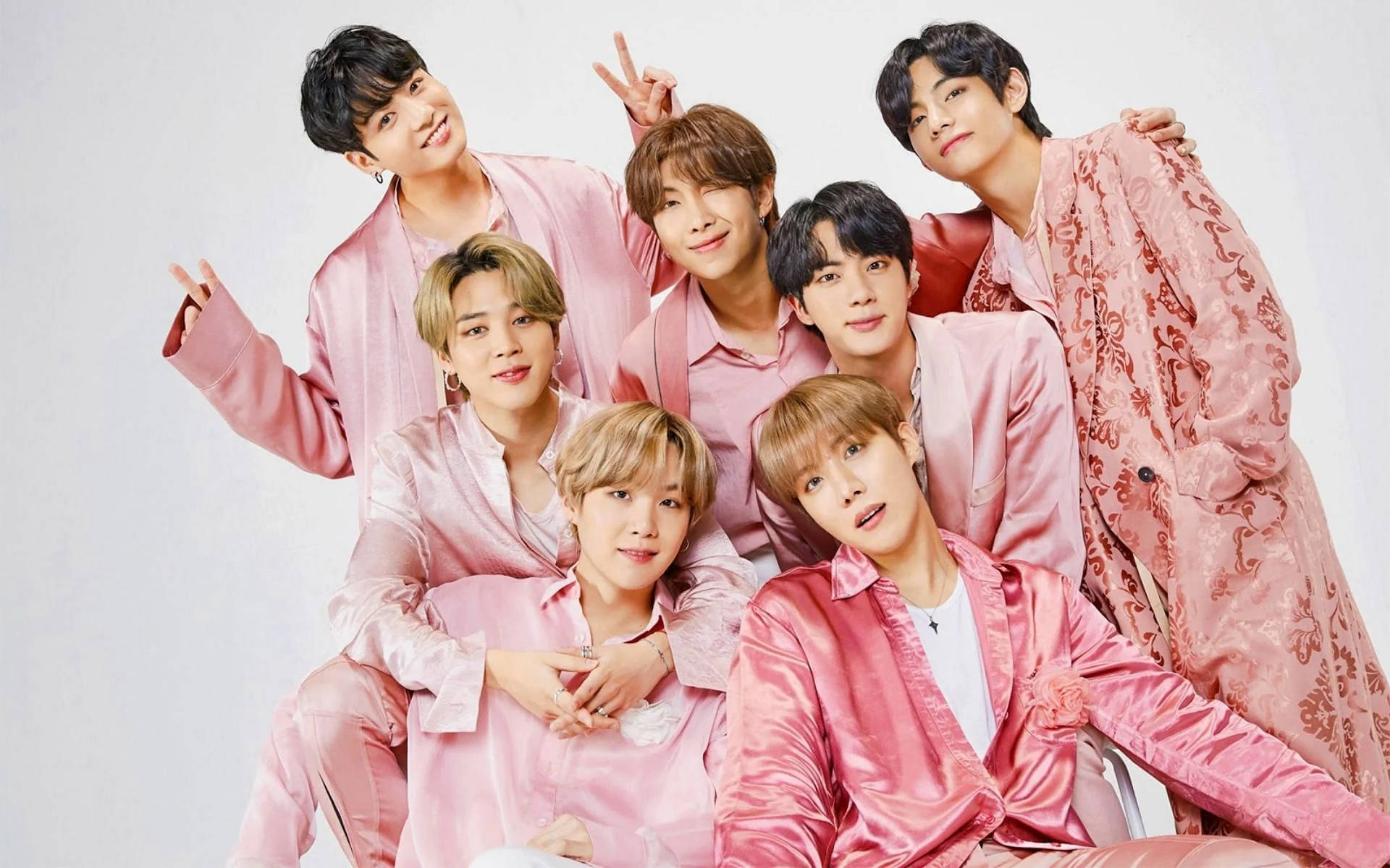 七名身穿粉紅色絲綢服裝的K-pop偶像在攝影棚中愉快地擺姿勢。 — Bts 壁紙
