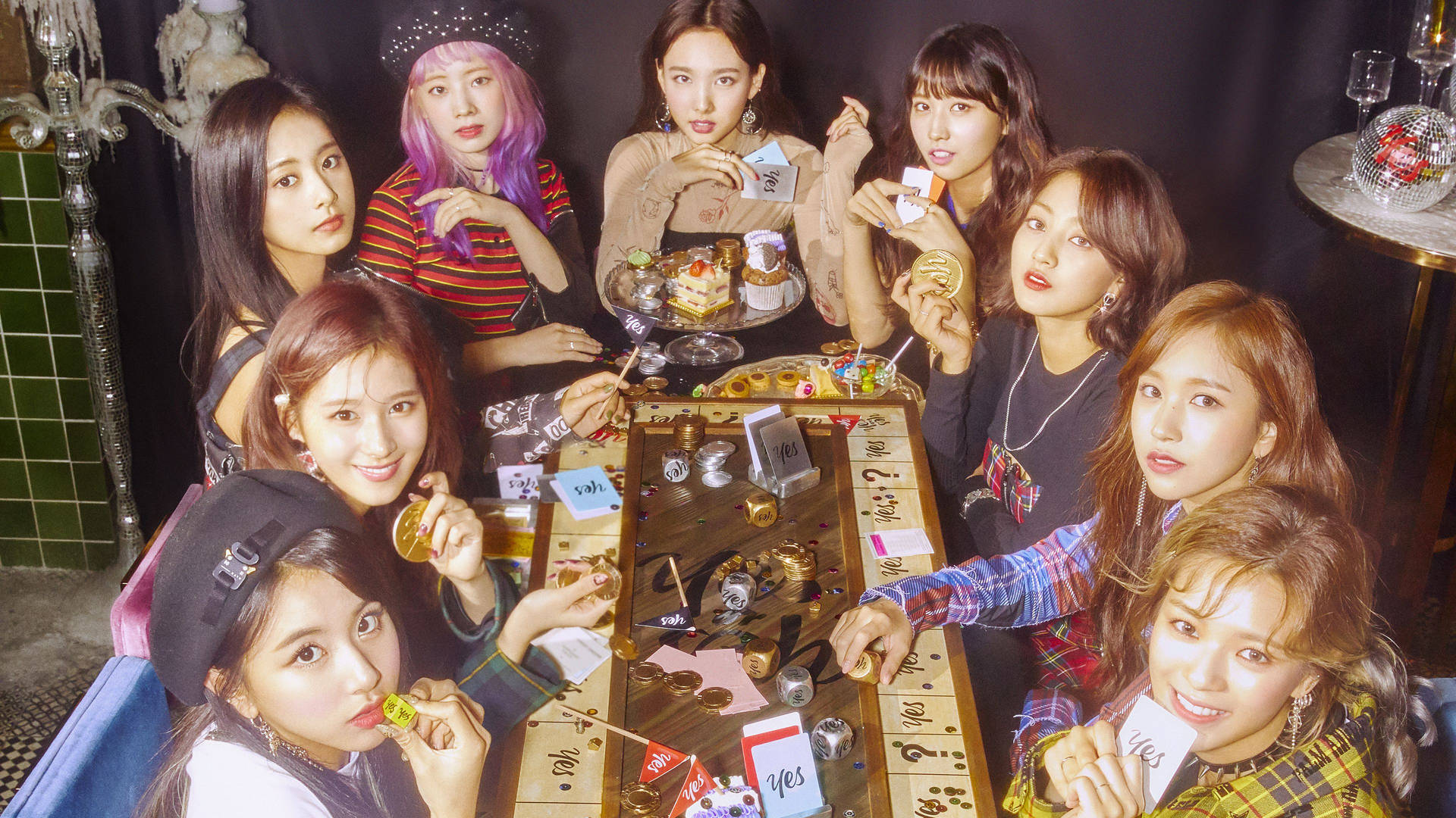 七位女性在光線昏暗、有迪斯科球的房間裡玩牌和吃零食。 — Twice 壁紙