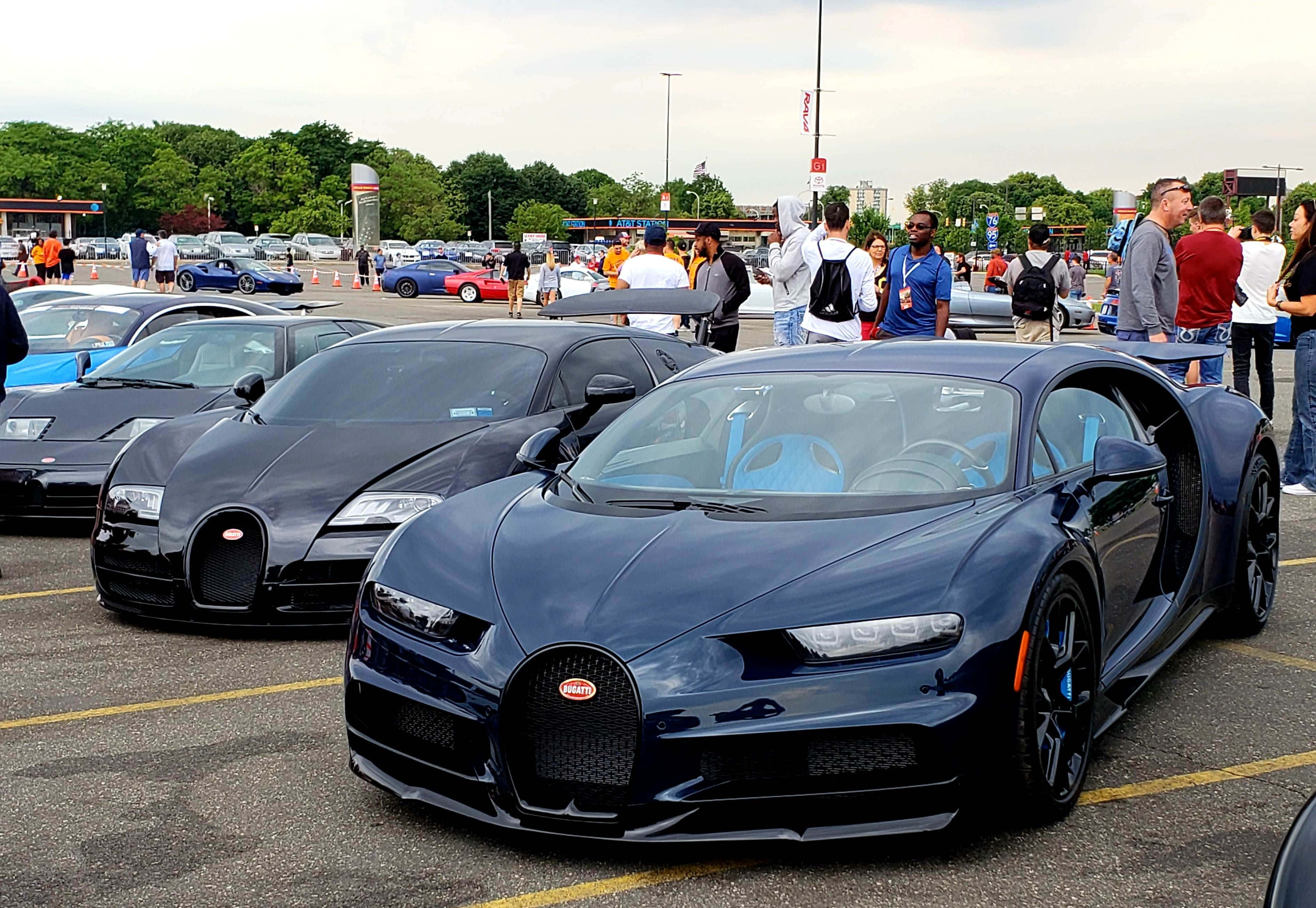 Bugatti Eb110 桌布 壁紙 — 閃亮的藍色和黑色Bugatti超級跑車停放在停車場，人群在陰天天空下欣賞它們。