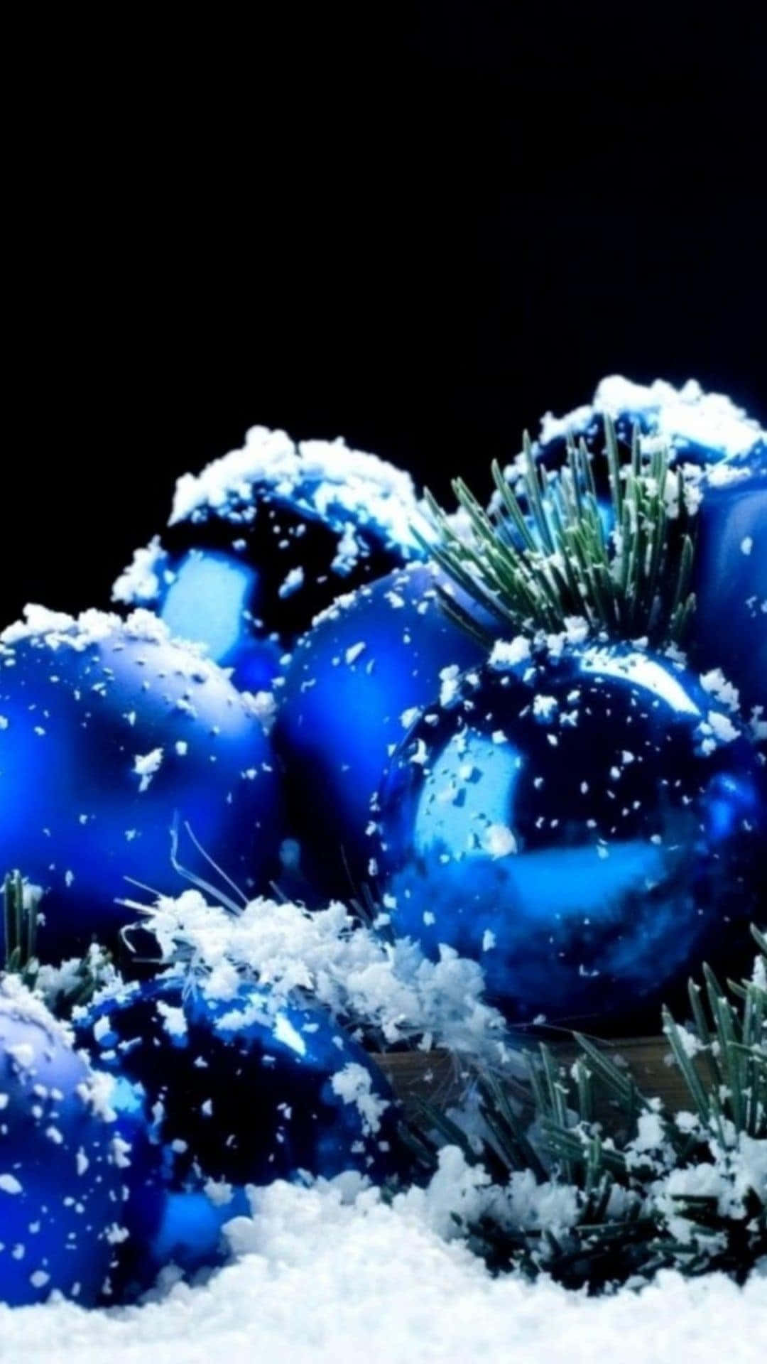  壁紙 — 閃亮的藍色聖誕裝飾品撒上雪花，躺在松針之間，背景為黑色。