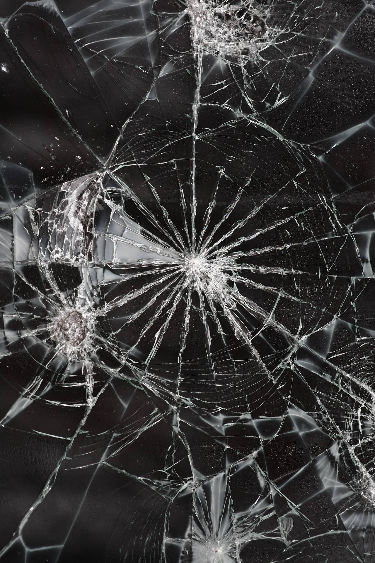 特寫破碎玻璃，在深色表面上呈現蜘蛛網狀裂紋。 — 裂屏 壁紙