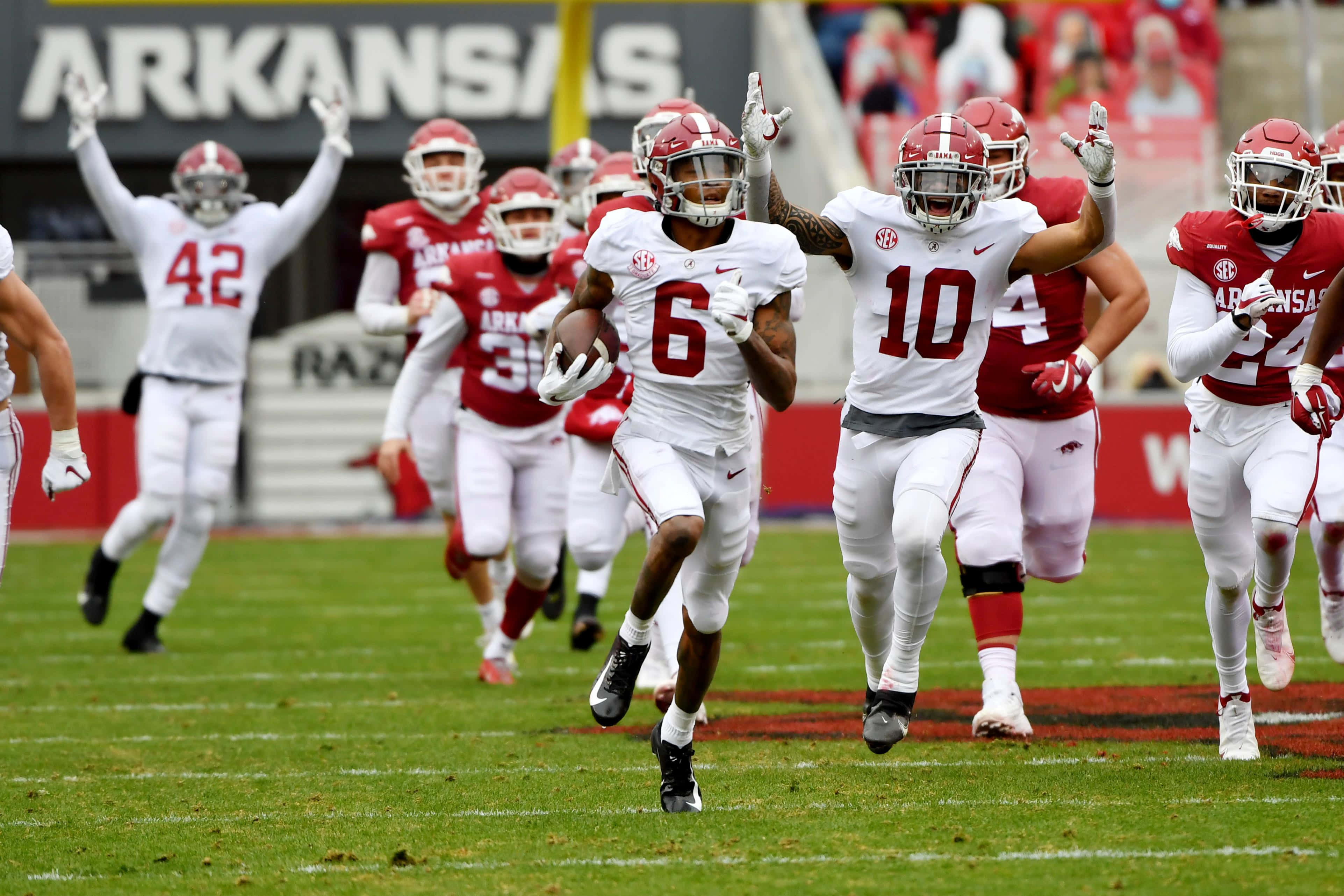Devonta Smith 桌布 壁紙 — 身穿白色和紅色球衣的足球運動員在明亮的日光下，於充滿活力的綠色球場上慶祝達陣。