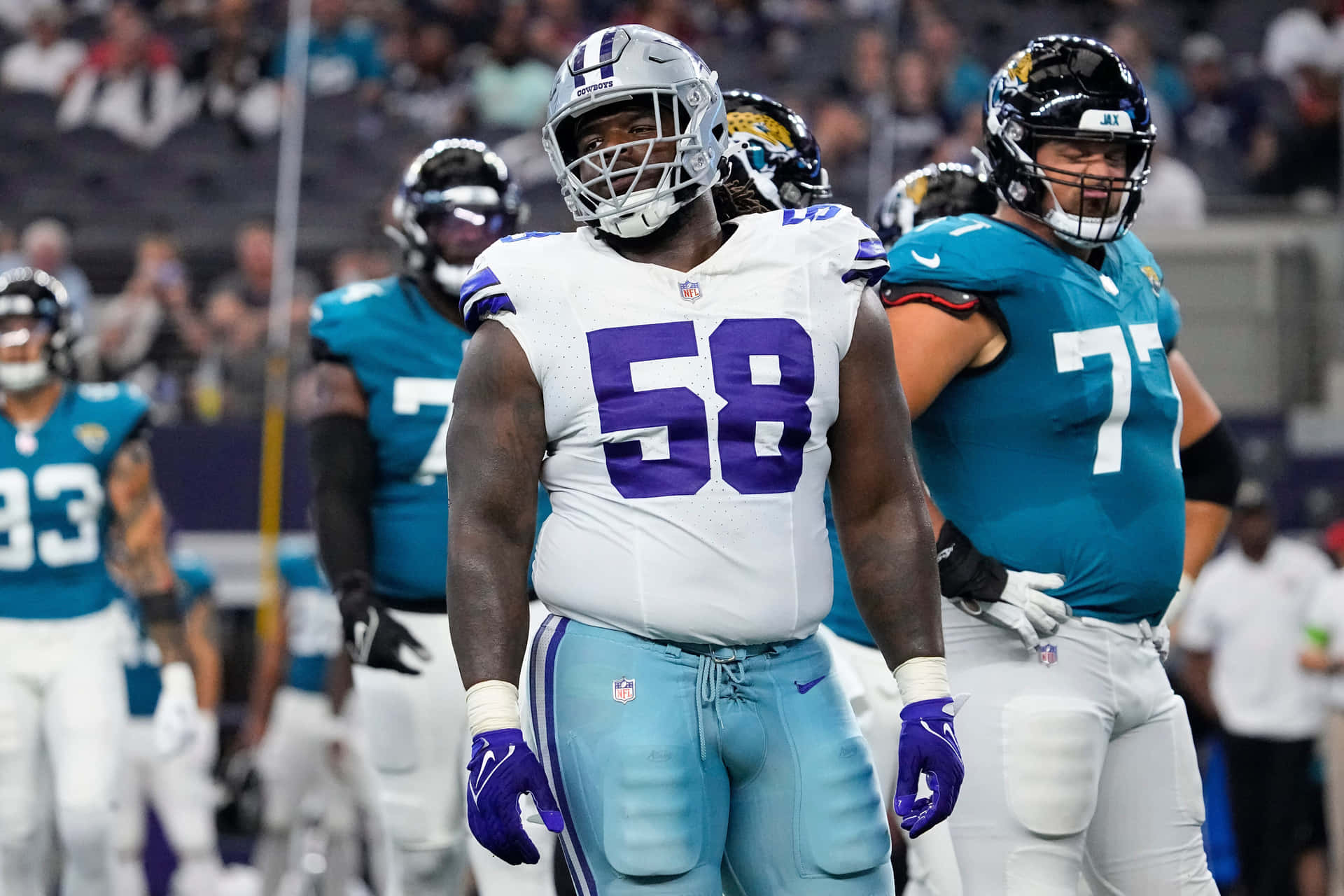  壁紙 — 身穿白色和藍綠色球衣的NFL美式足球員在明亮的燈光下，於比賽期間站在體育場上。