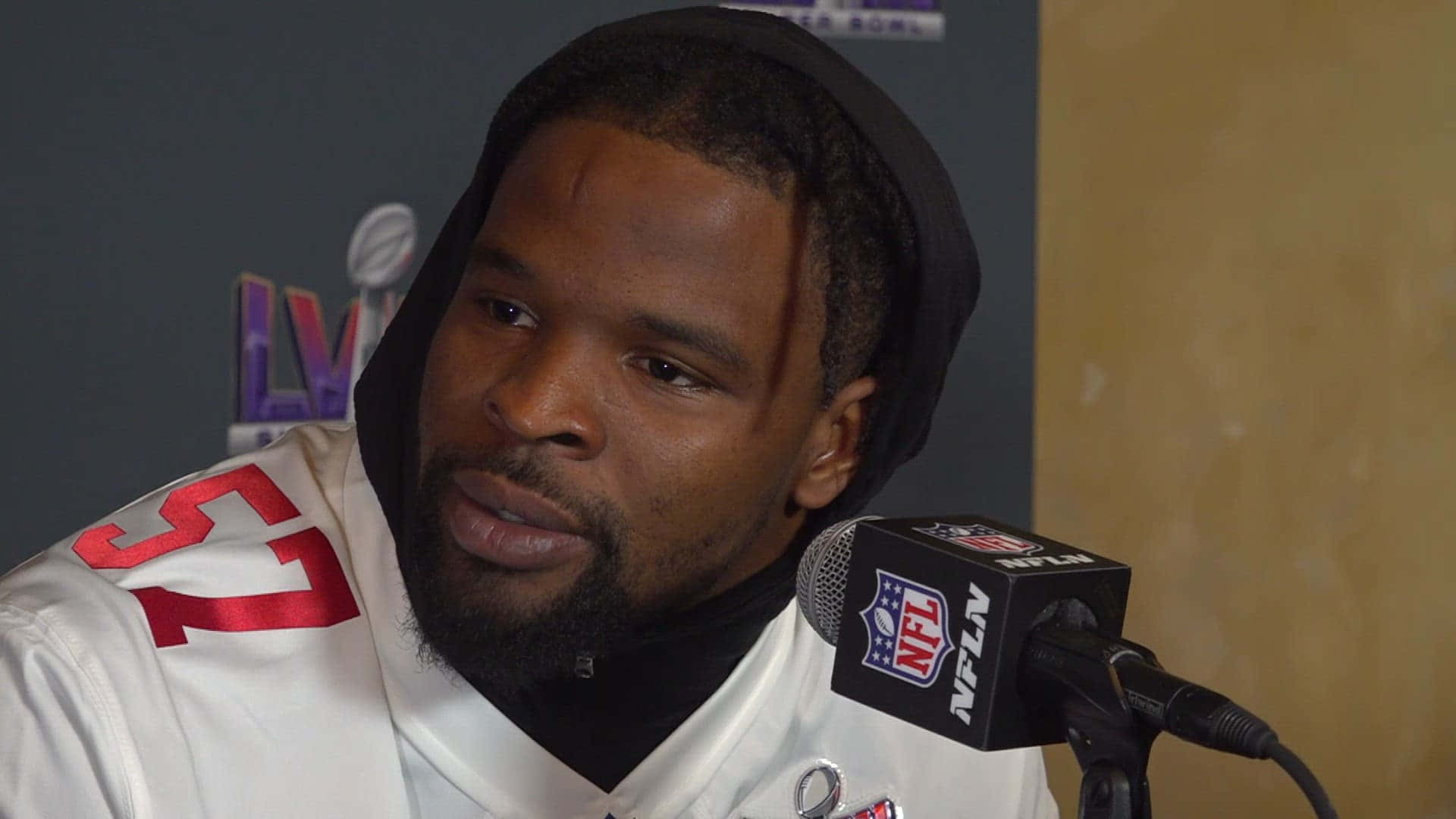  壁紙 — 身穿白色球衣的NFL球員在記者會上對著麥克風發言，背景為LV標誌。