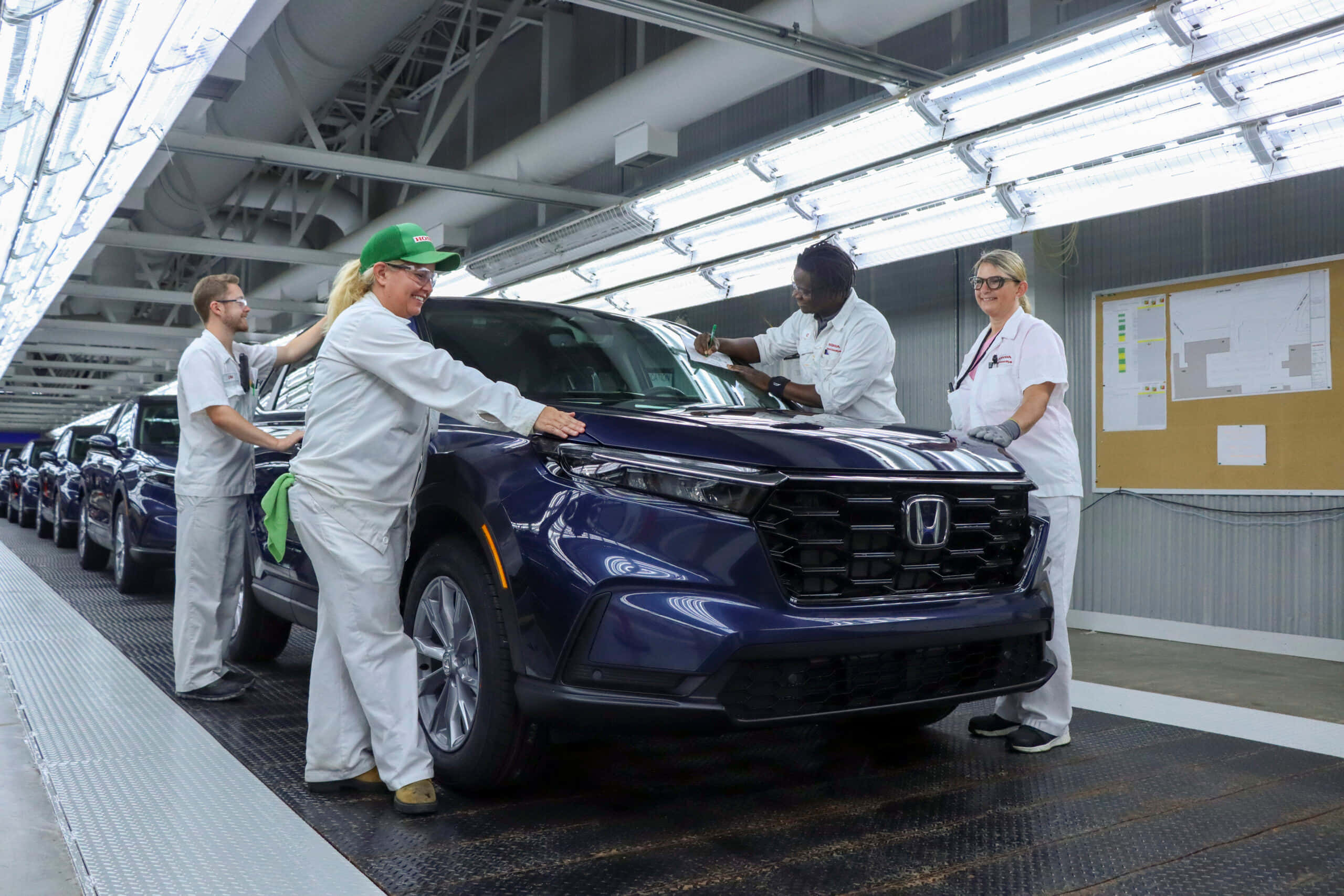 Honda Cr-v 桌布 壁紙 — 身穿白色制服的工廠工人在明亮的螢光燈下檢查裝配線上的光面藍色本田SUV。