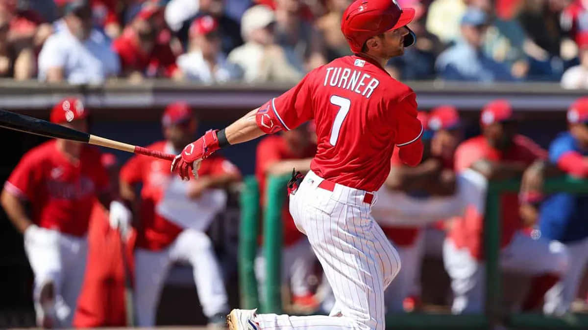 Trea Turner Phillies 桌布 壁紙 — 身穿紅色球衣的棒球手Turner在揮棒中途，背景有觀眾。