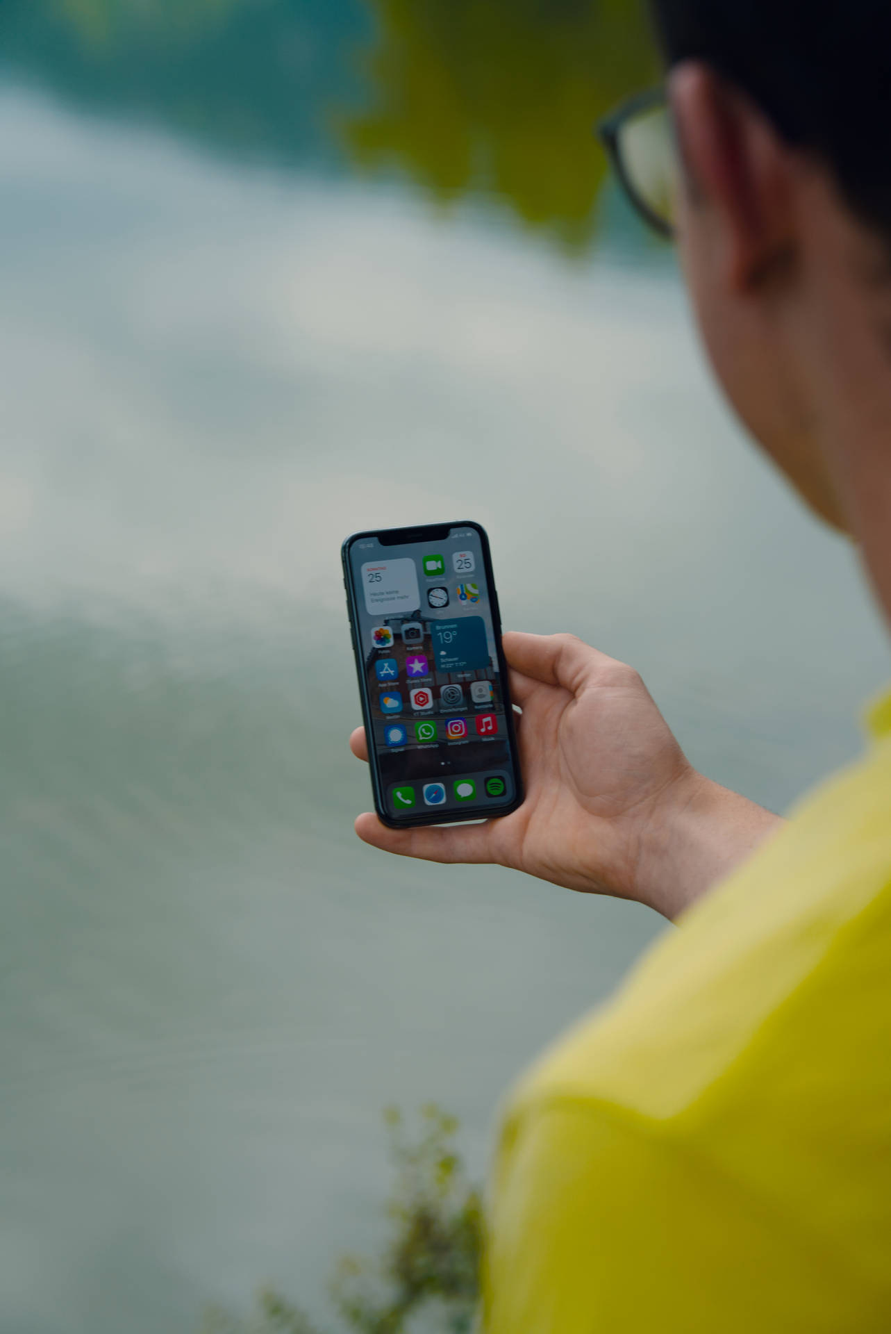身穿黃色襯衫的人在水邊手持電話 — iOS 16 壁紙 壁紙