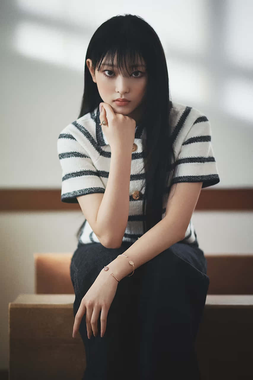  壁紙 — 一位長黑髮的年輕女性穿著條紋針織上衣和深色褲子，若有所思地坐在木階梯上。
