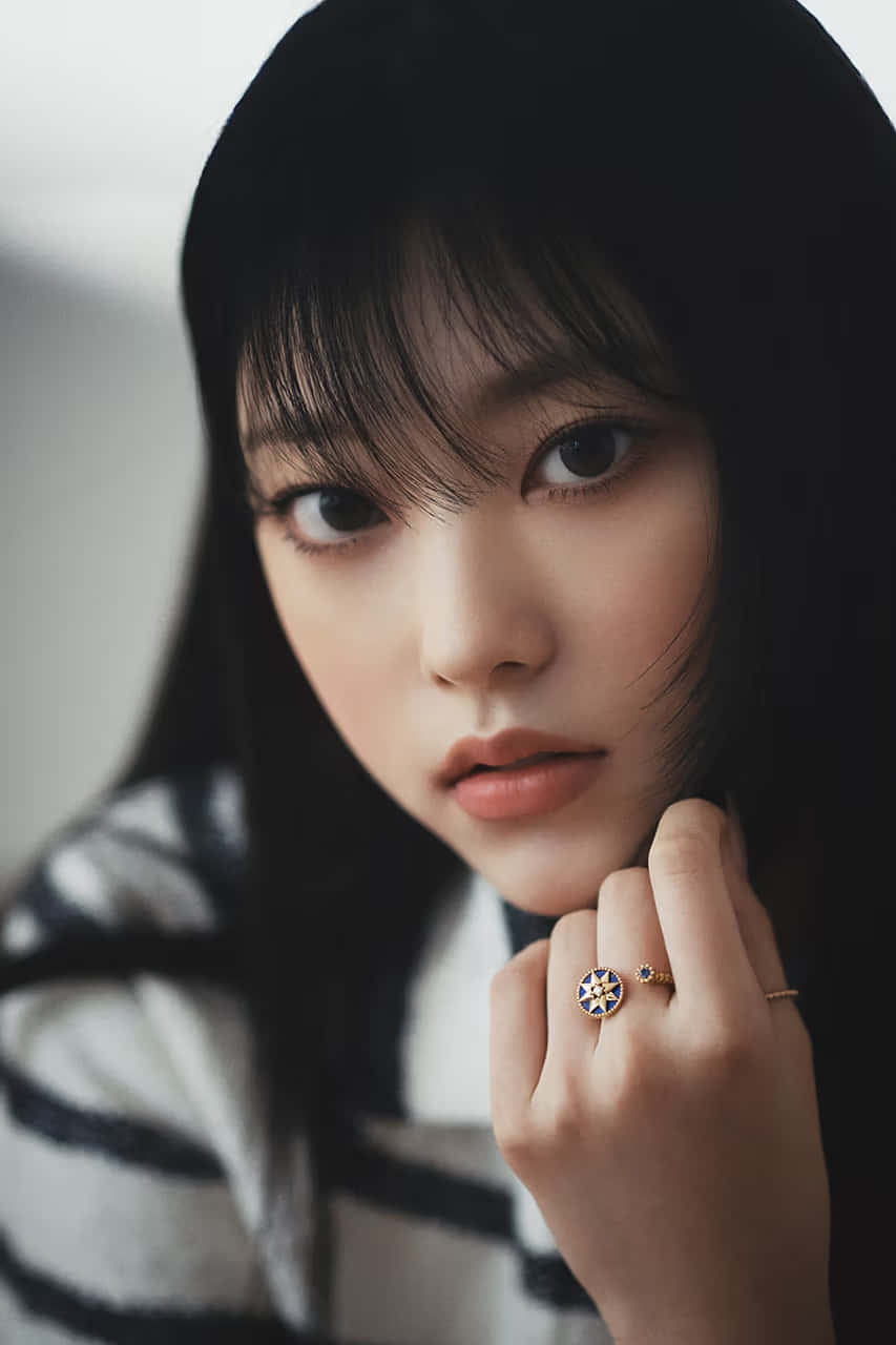  壁紙 — 一位深色頭髮、化著柔和妝容的年輕女性，將下巴擱在戴著戒指的手上，直視鏡頭。
