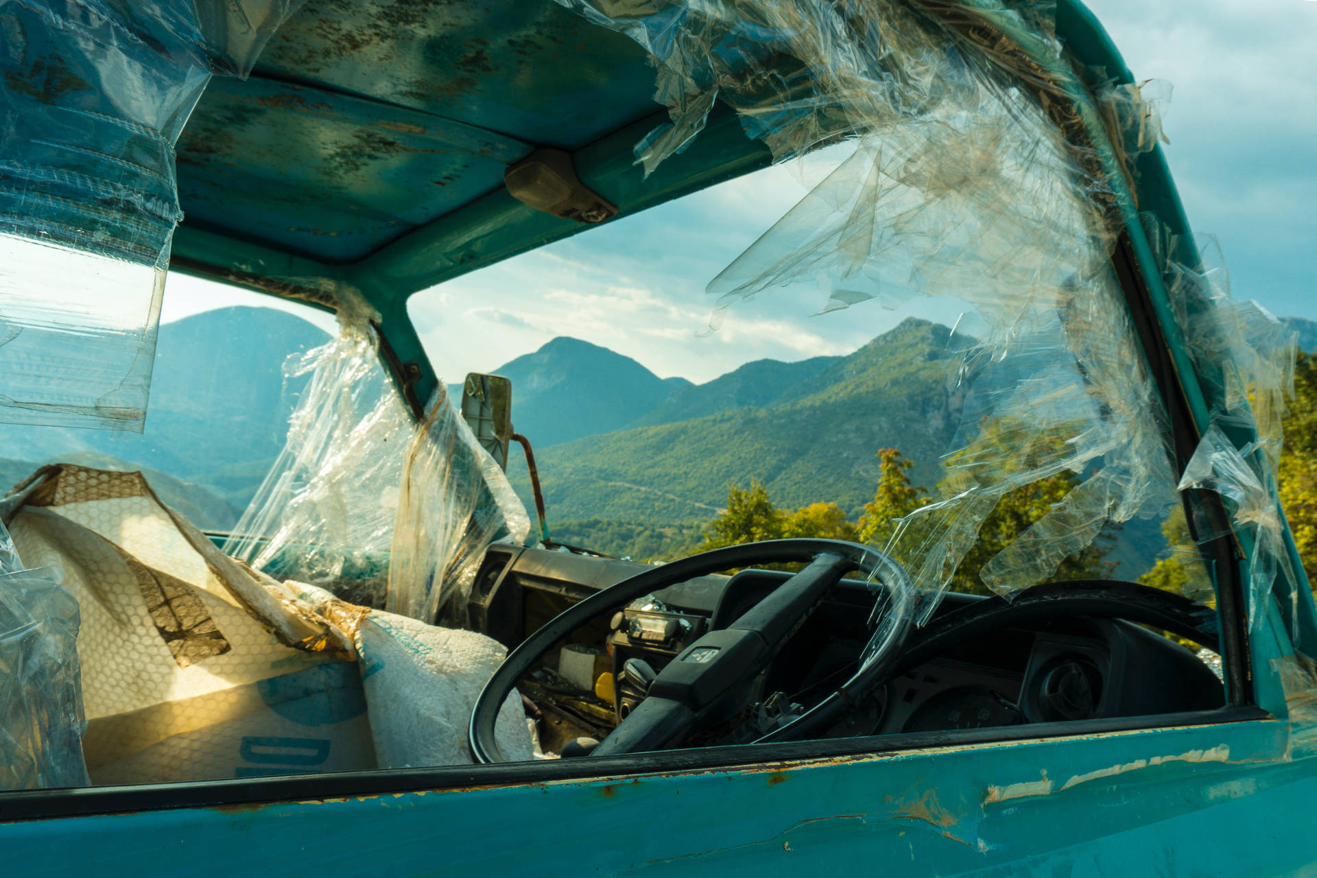 廢棄的藍綠色卡車，破損的塑膠車窗俯瞰著綠色的山脈。 — 車禍 壁紙