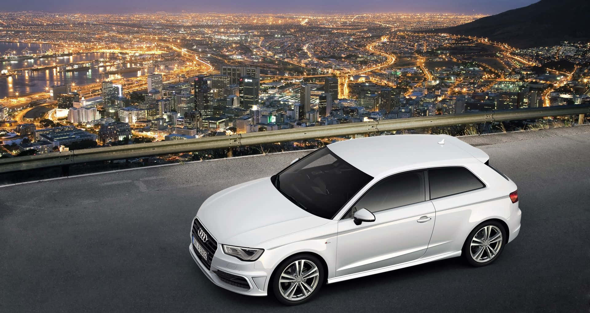 Audi A3 桌布 壁紙 — 一輛時尚的白色奧迪停在一個山丘上，俯瞰著一片被金色夜燈照亮、廣闊的城市景觀。