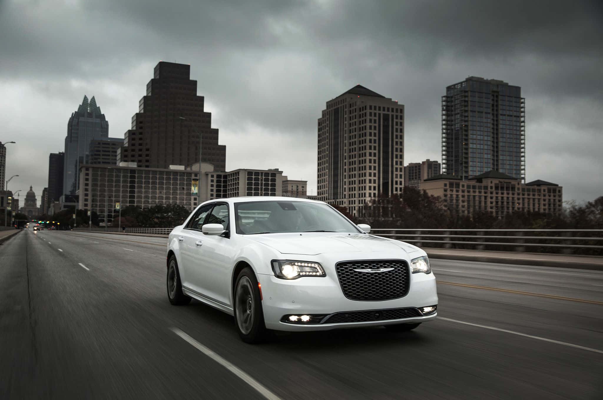 Chrysler 300 桌布 壁紙 — 一輛時尚的白色轎車在城市的橋上行駛，背景是陰沉的灰色雲層和摩天大樓。
