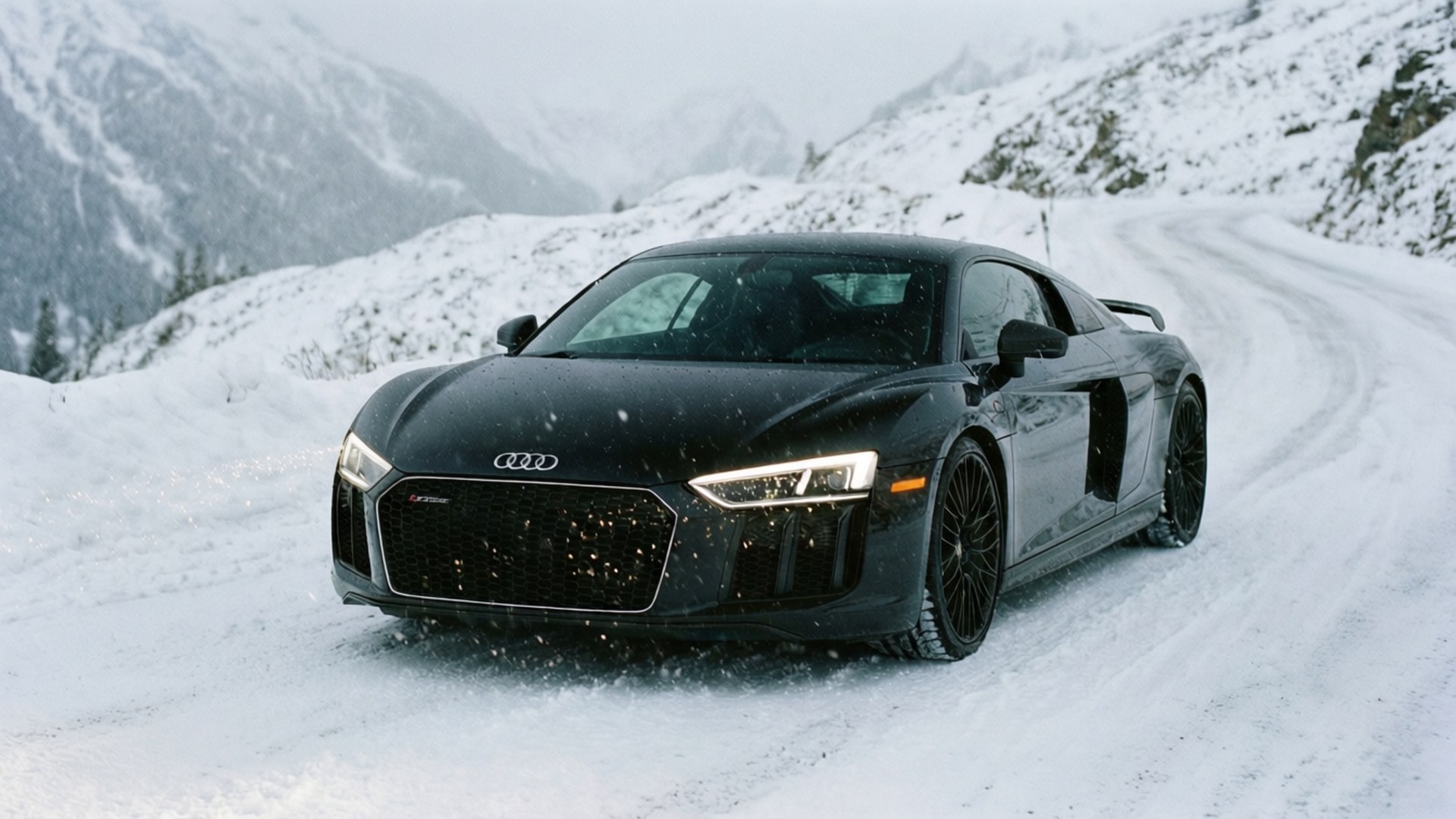Snowy R8 壁紙 — 一輛時尚的黑色奧迪R8跑車在雪花飄落的雪山上行駛。