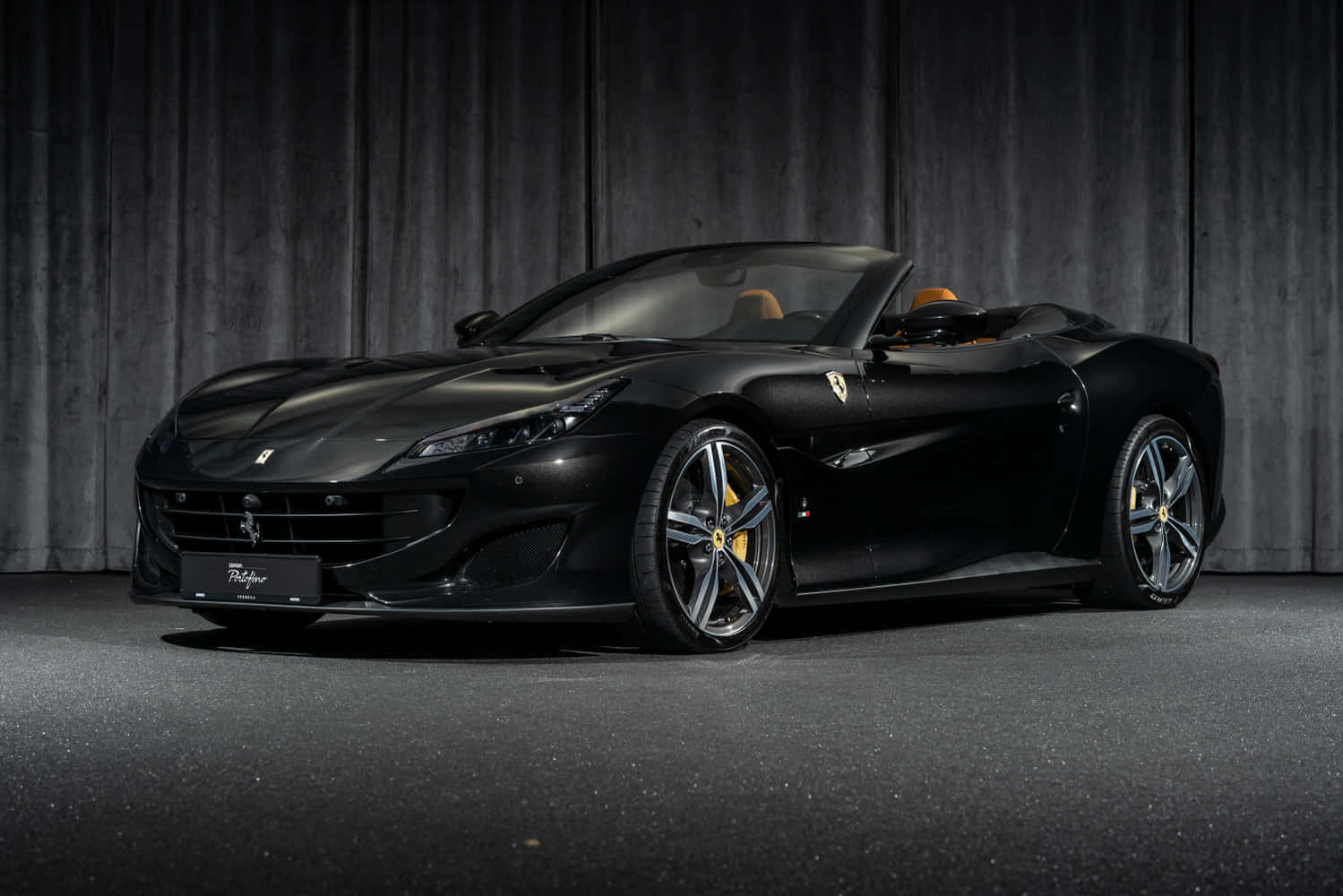 Ferrari Portofino 桌布 壁紙 — 一輛時尚的黑色法拉利 Portofino 敞篷車，配備米色內裝，在工作室燈光下，停在深色木質背景前。