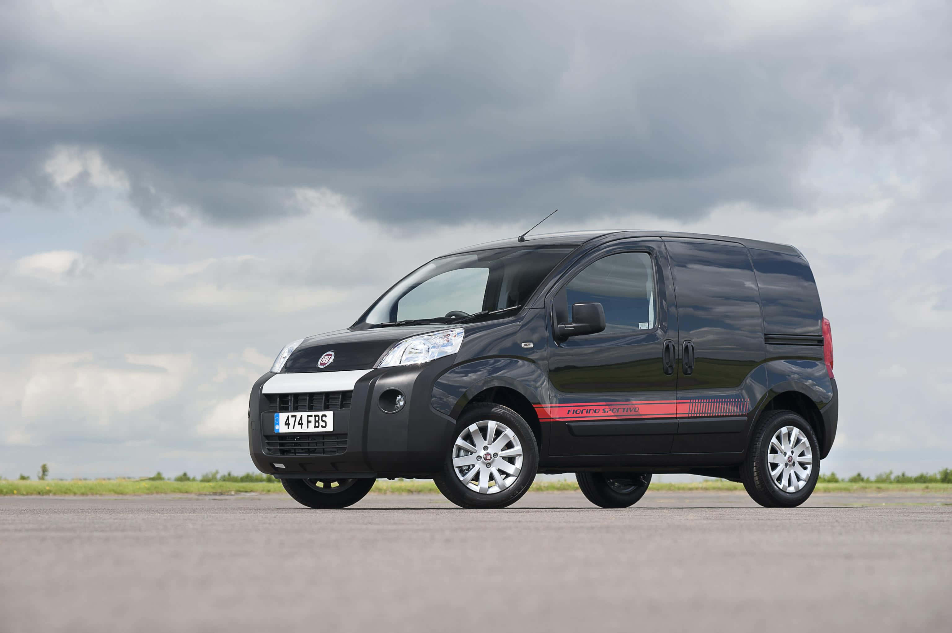 Fiat Fiorino 桌布 壁紙 — 一輛時尚的黑色Fiat Fiorino廂型車帶有紅色賽車條紋，停在開闊的柏油路面上，天空多雲。
