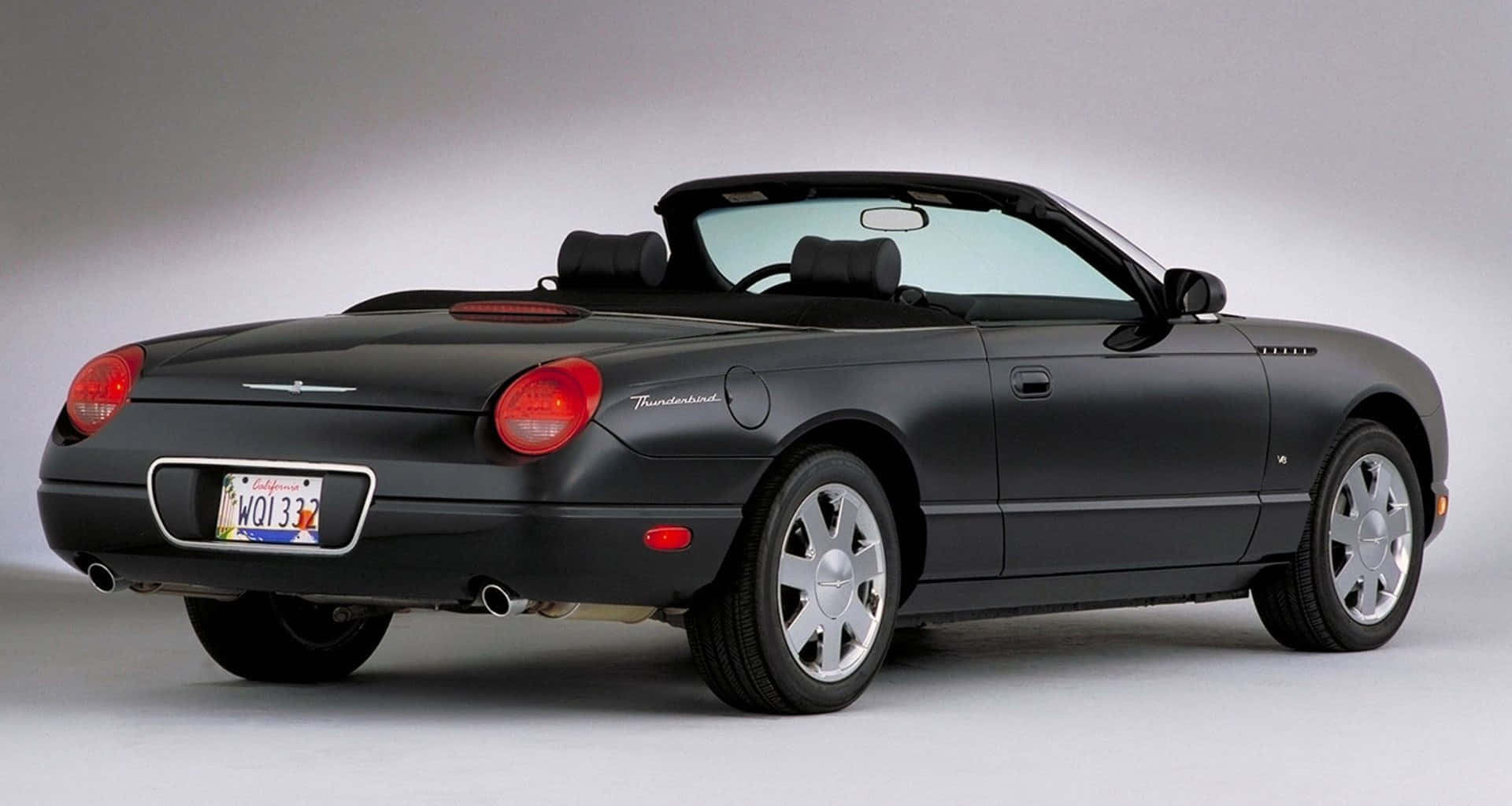 Ford Thunderbird 桌布 壁紙 — 一輛時尚的黑色福特雷鳥敞篷車，帶有紅色尾燈和銀色輪圈，擺放在中性灰色工作室背景前。