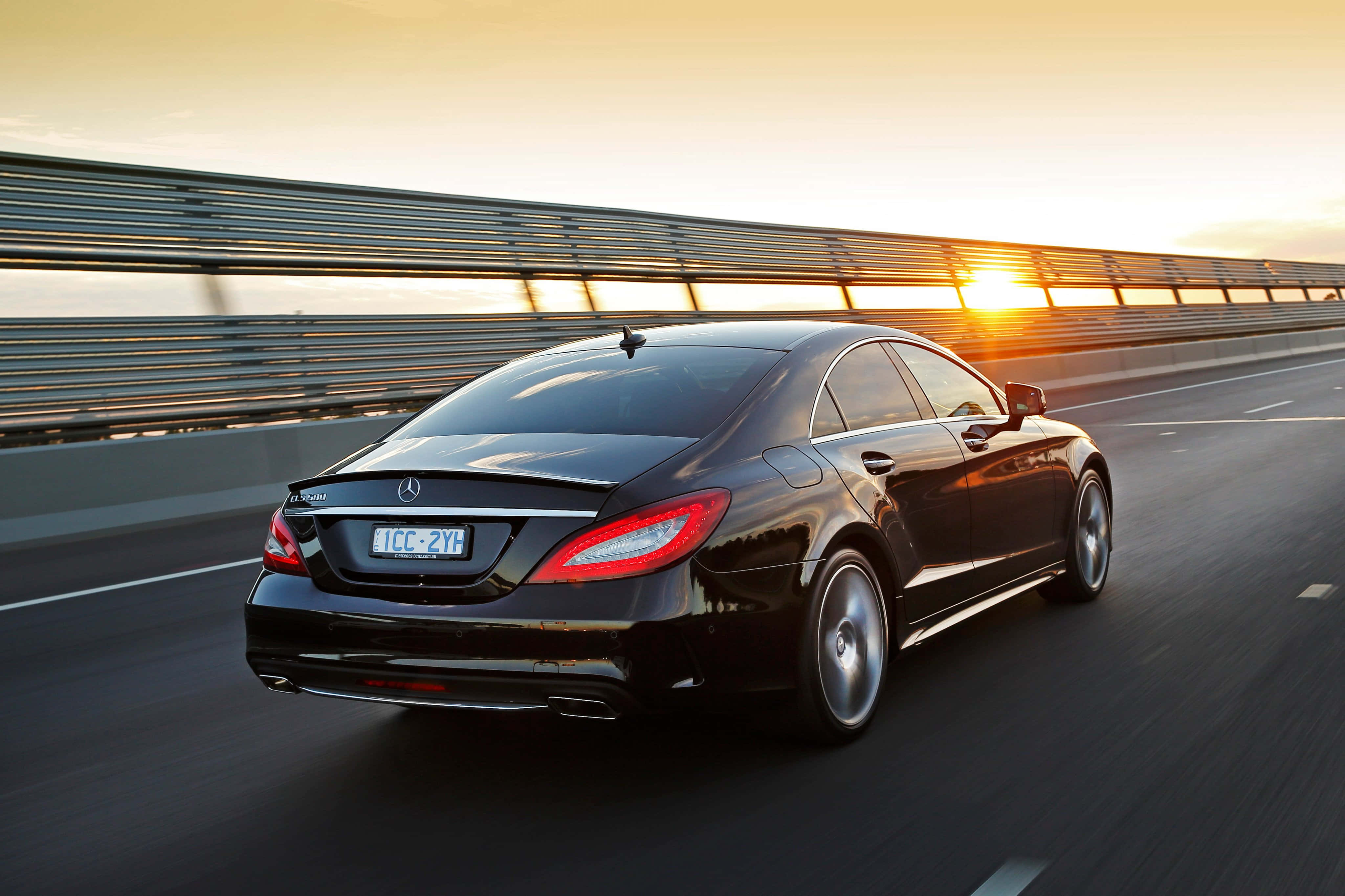 Mercedes Benz Cls-class 桌布 壁紙 — 一輛時尚的黑色Mercedes CLS Coupe在日落時分沿高速公路疾馳，金色光線反射在其光滑表面上。