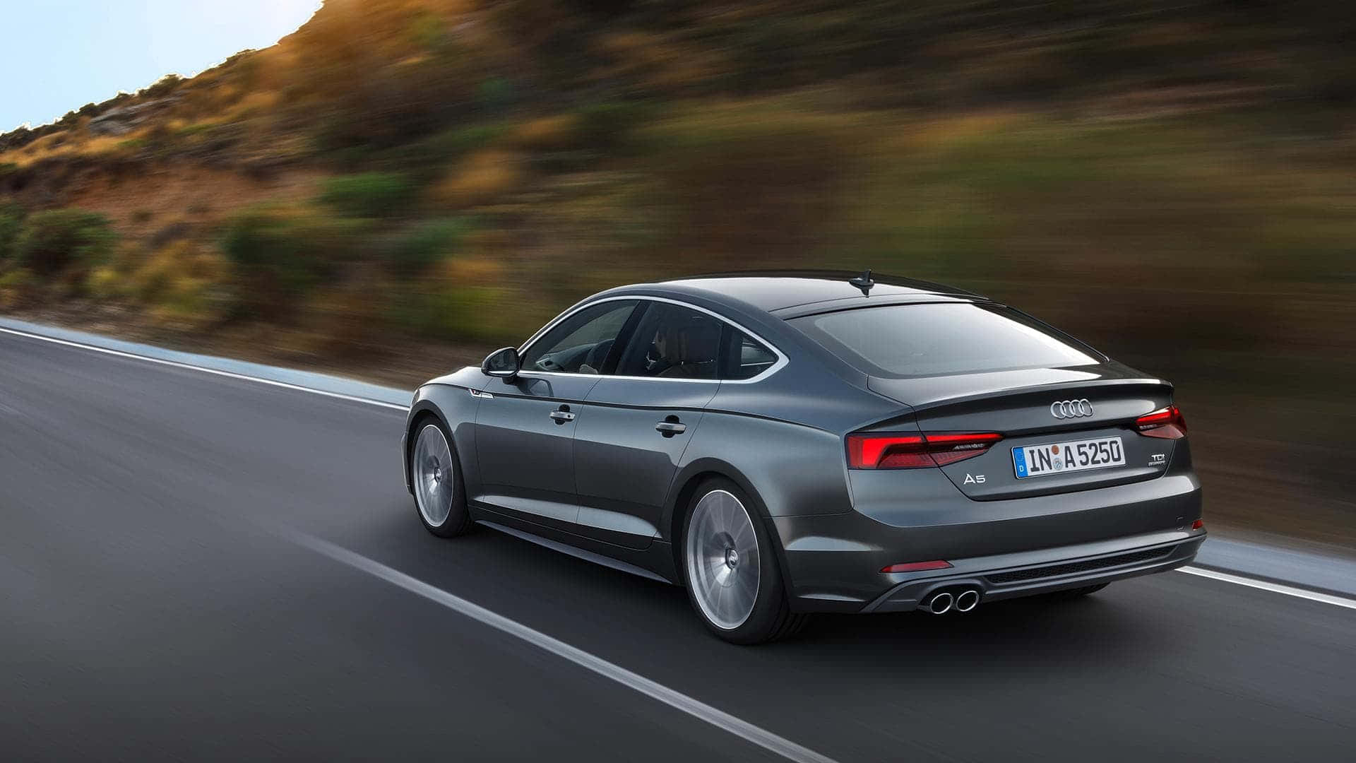 Audi A5 桌布 壁紙 — 一輛時尚的灰色奧迪A5跑車沿著蜿蜒的山路疾馳，模糊的綠色在移動中。