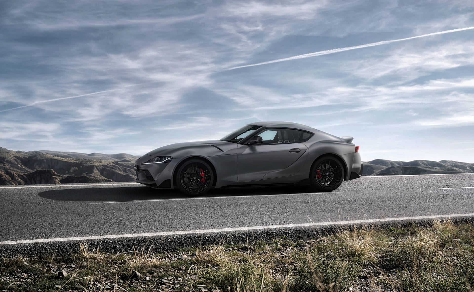 灰色跑車在多雲天空下行駛在山路上 — Toyota Supra 壁紙