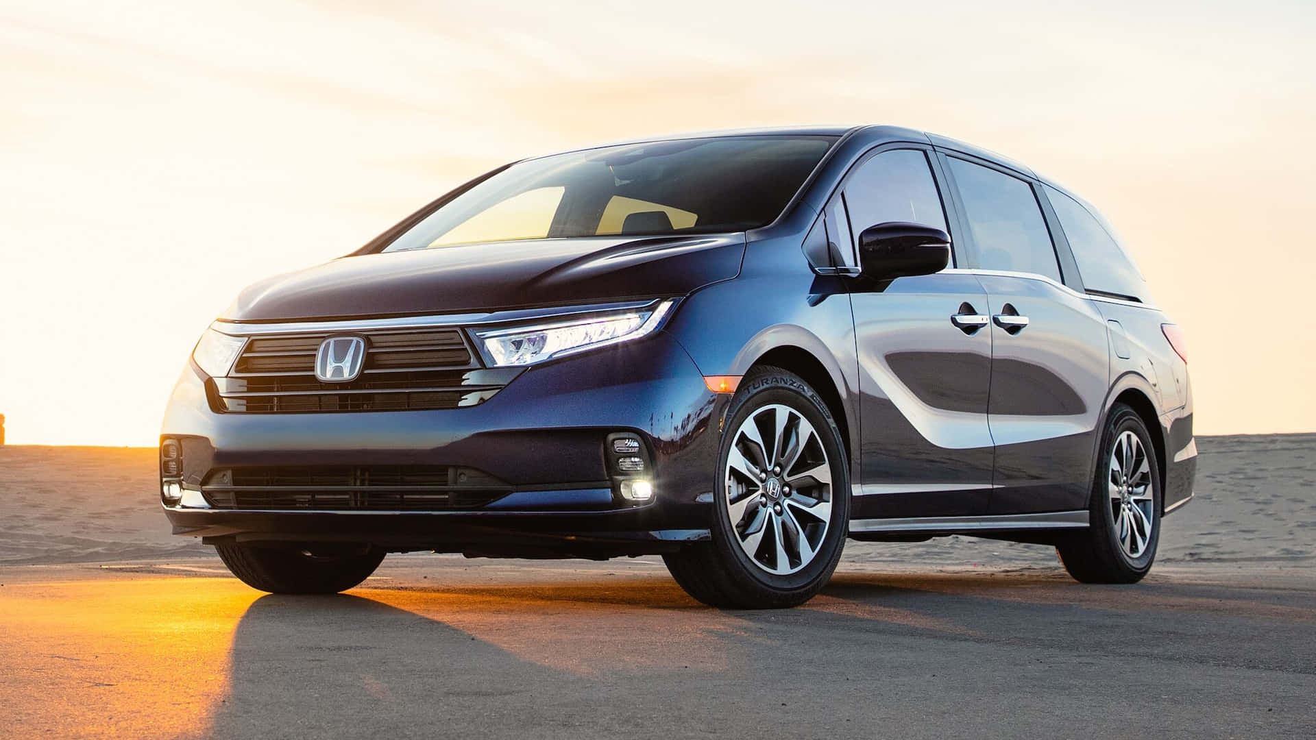 Honda Odyssey 桌布 壁紙 — 一輛時尚的藍色本田廂型車在沙漠公路上閃耀著金色的日落光芒。