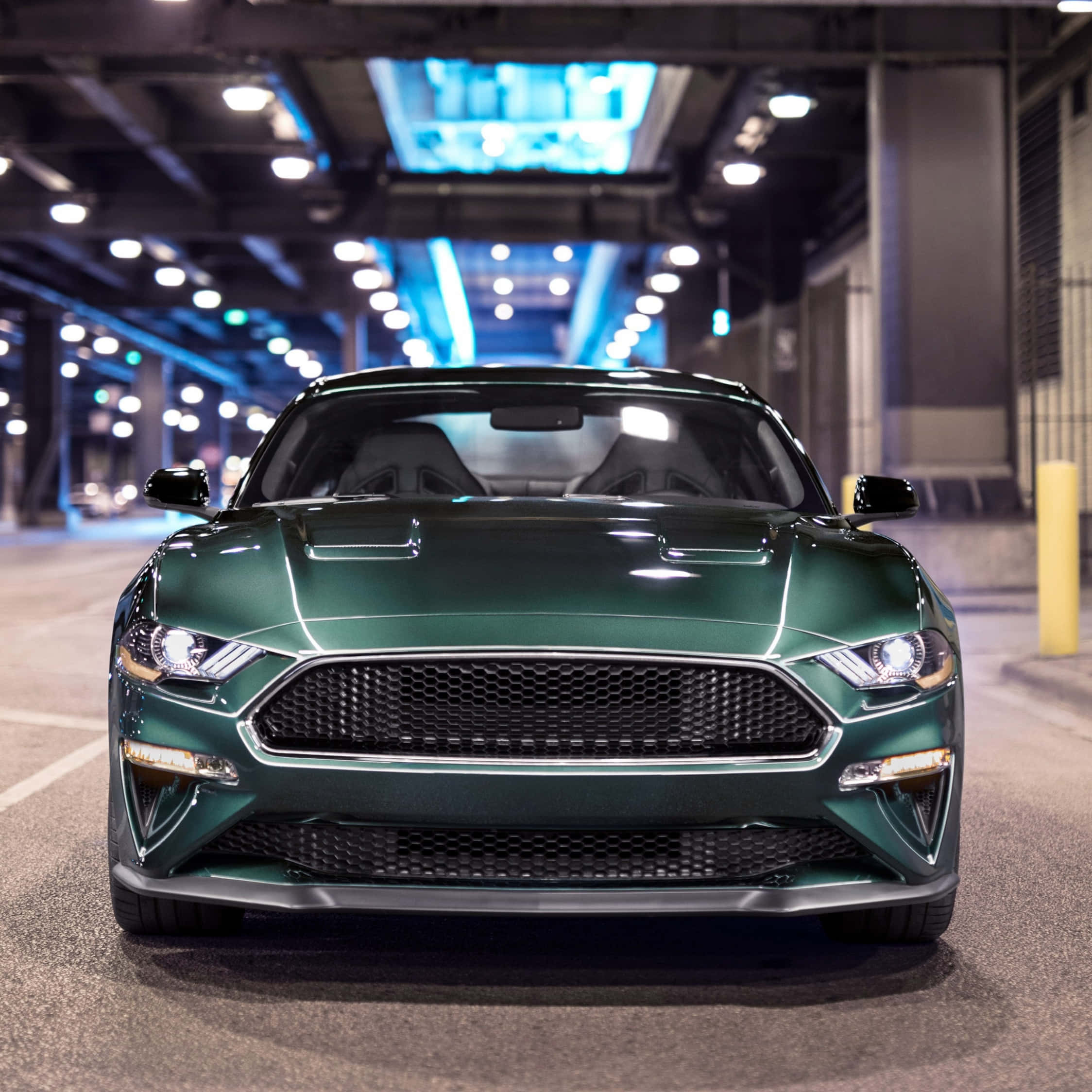 Ford Mustang Bullitt 桌布 壁紙 — 一輛時尚的綠色福特野馬在燈光昏暗的地下停車場中向前，頭頂有藍色燈光。