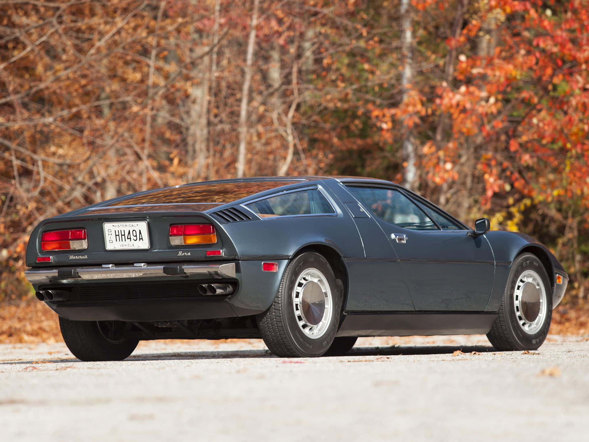 Maserati Bora 桌布 壁紙 — 一輛時尚的深灰色瑪莎拉蒂Merak跑車停在碎石路上，周圍是充滿活力的秋葉。