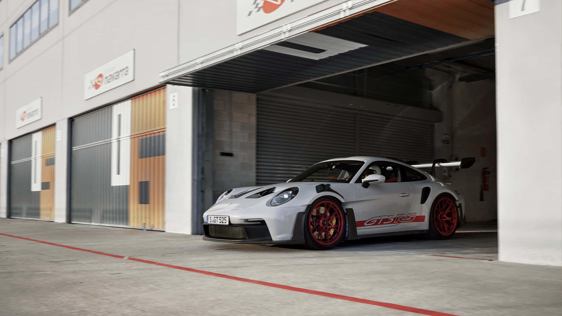  壁紙 — 一輛時尚的銀色保時捷911 GT3 RS，帶有紅色點綴和輪圈，停在現代工業車庫前。