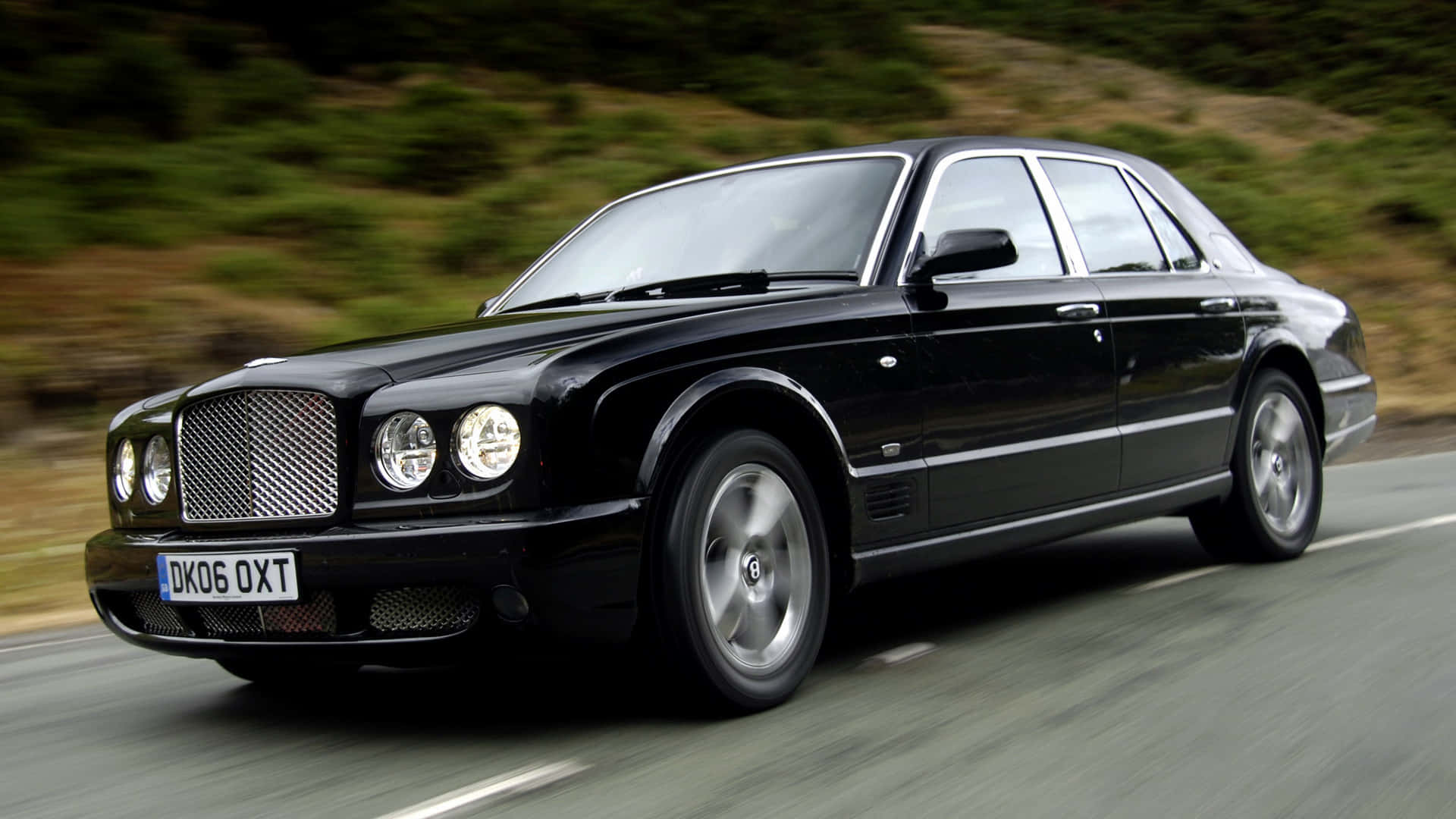 Bentley Arnage 桌布 壁紙 — 一輛時尚的黑色賓利轎車沿著蜿蜒的道路疾馳，背景是模糊的綠色山丘。