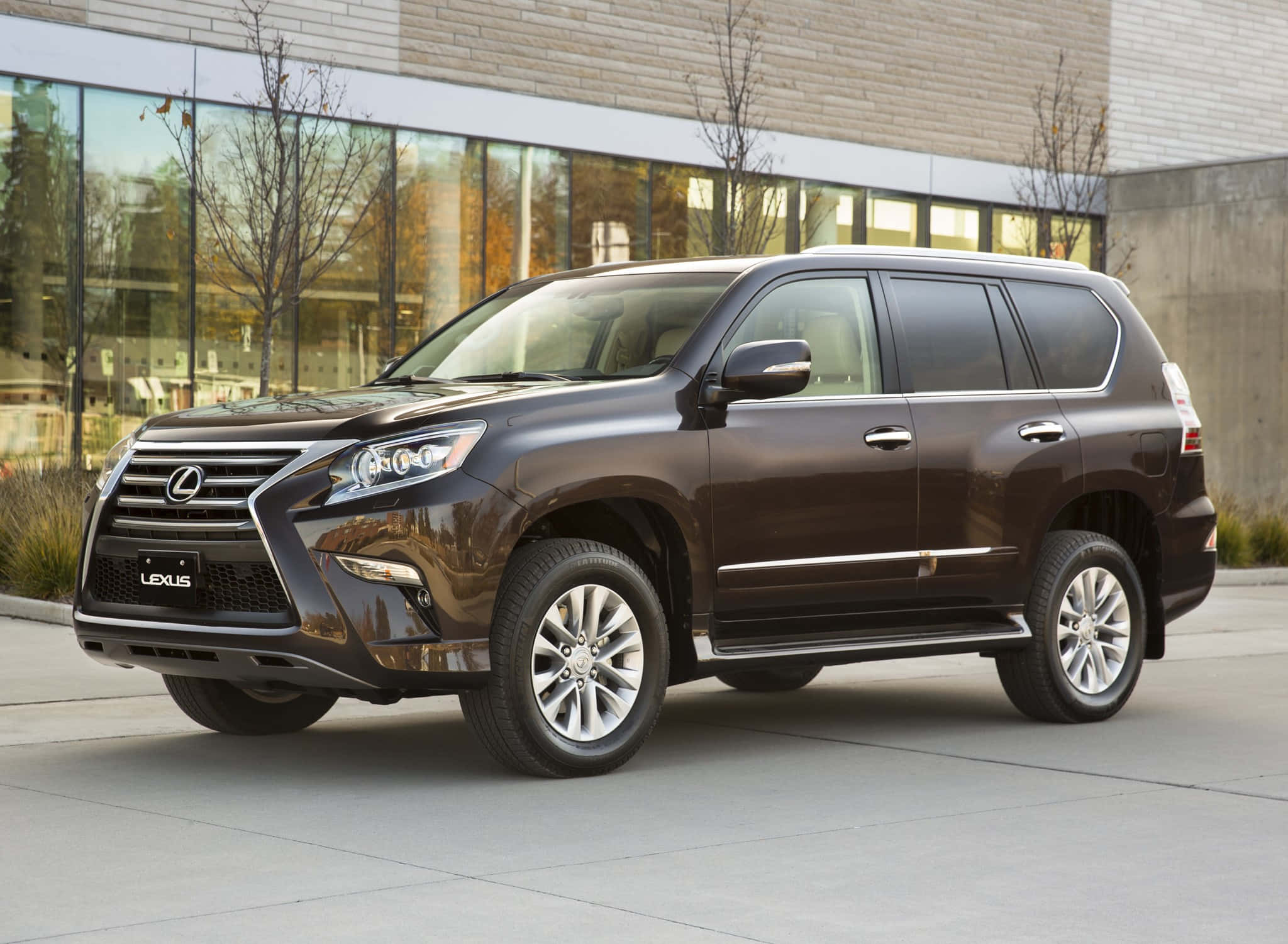 Lexus Gx 460 桌布 壁紙 — 一輛時尚深棕色Lexus GX SUV停放在玻璃和磚砌建築前的現代混凝土廣場上。