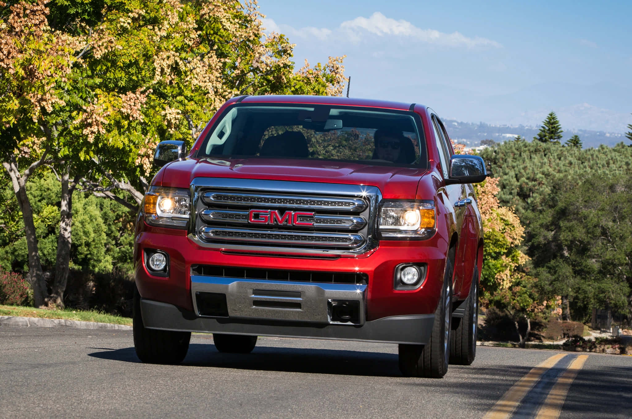 Gmc Canyon 桌布 壁紙 — 一輛閃亮的紅色GMC皮卡車在藍天白雲下，沿著綠樹成蔭的道路行駛。