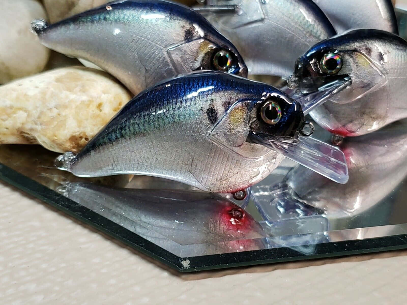  壁紙 — 閃亮的銀色沙丁魚形魚餌，帶有玻璃眼睛，放置在反光玻璃表面上，旁邊有一塊淺色石頭。