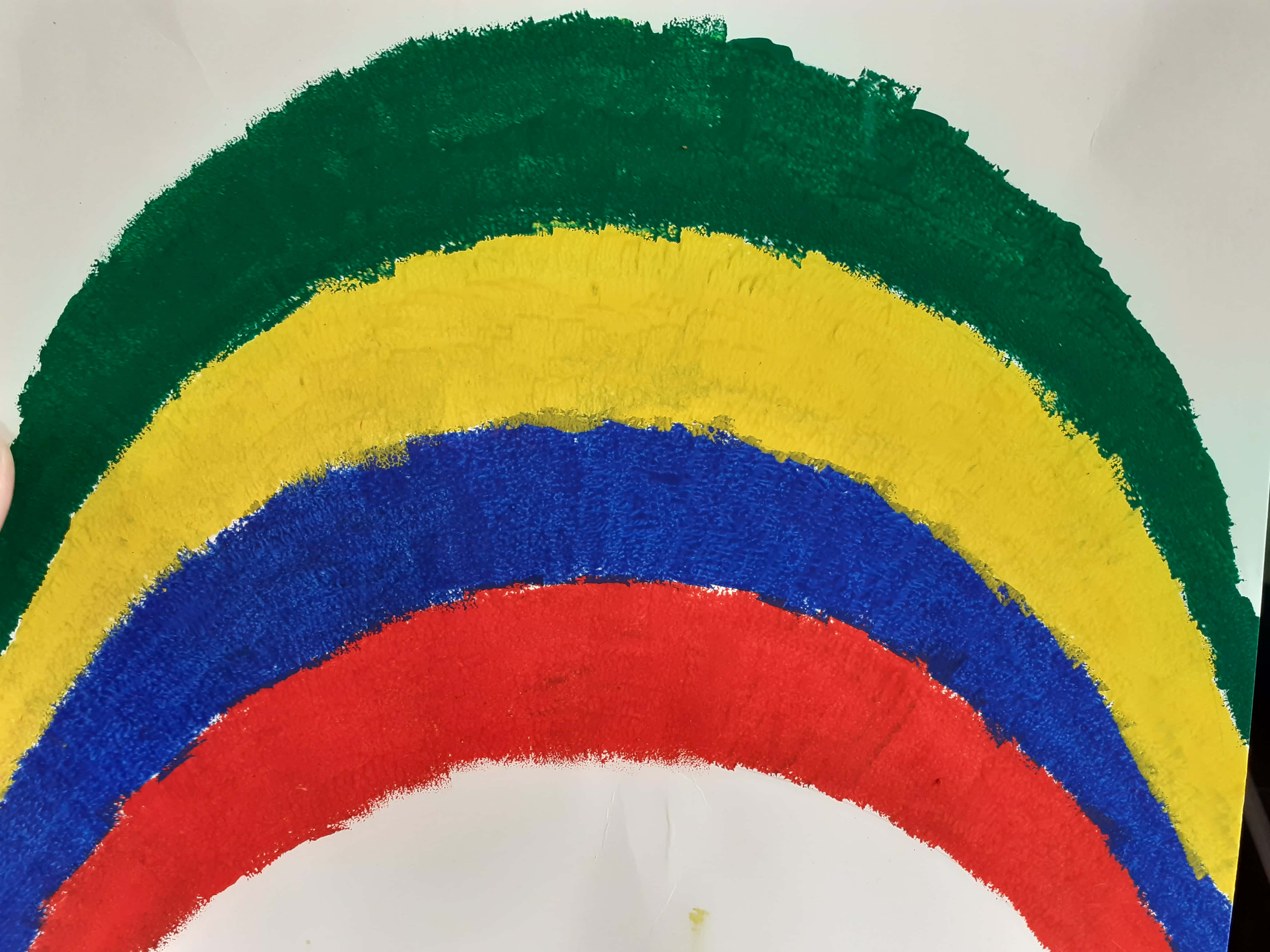 Rainbow Art 桌布 壁紙 — 一條充滿活力的手繪彩虹，以綠色、黃色、藍色和紅色的厚實紋理筆觸橫跨白紙。