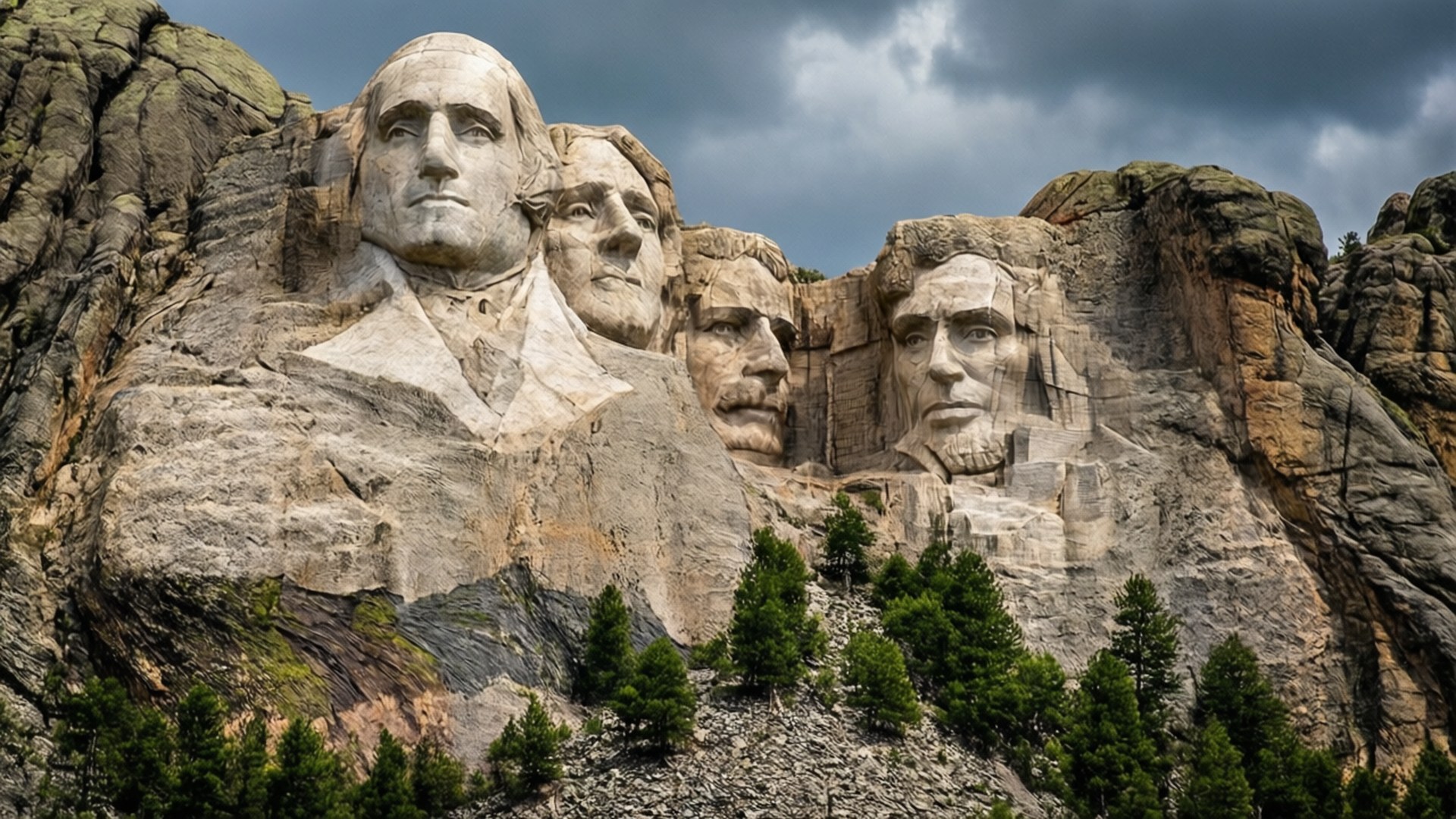 Mount Rushmore Majesty 壁紙 — 四個巨大的總統面孔雕刻在崎嶇的山上，背景是戲劇性的多雲天空，底部有常青樹。