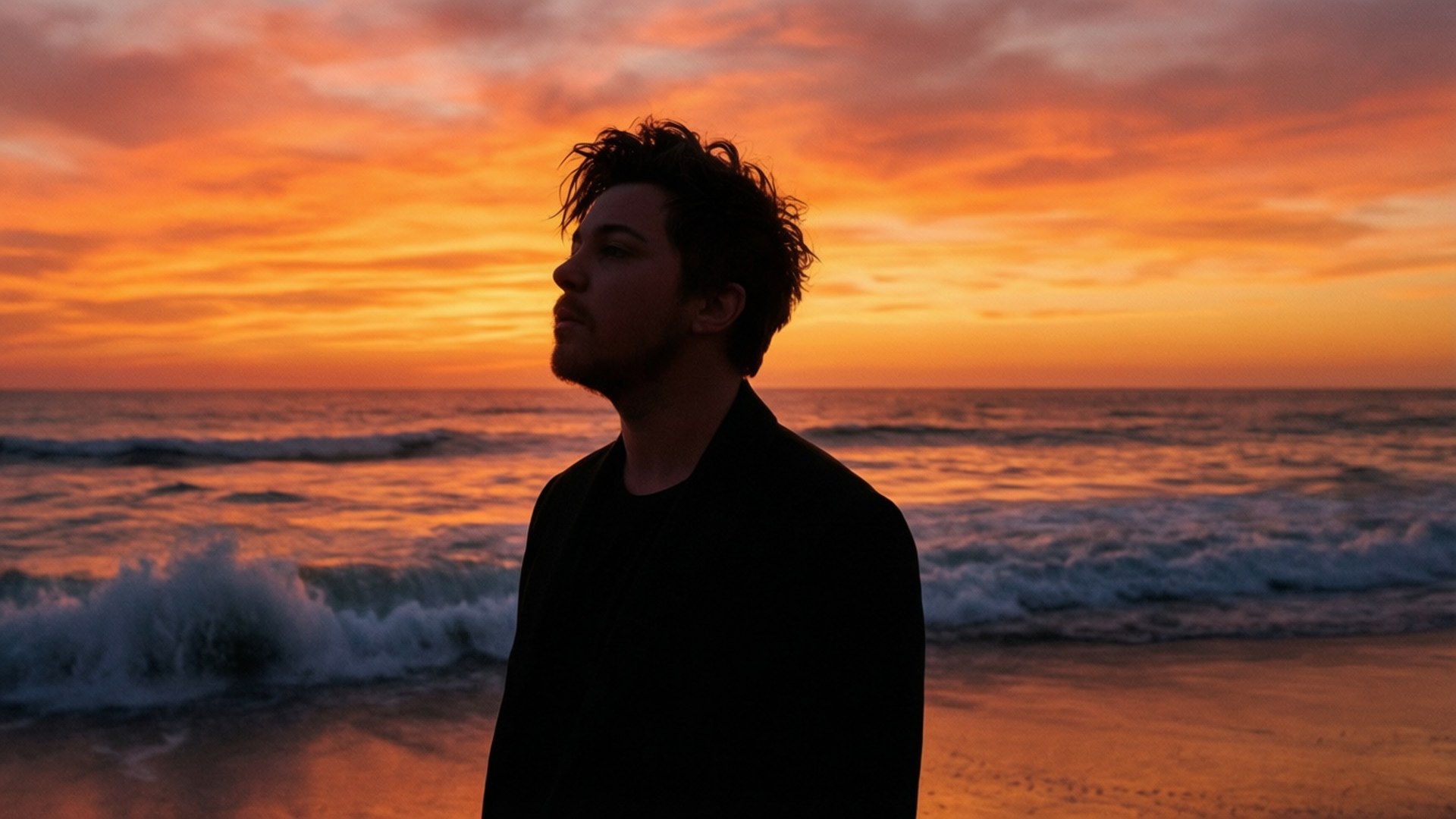 Beach Sunset Silhouette 壁紙 — 一個男人以剪影站在沙灘上，海浪在火熱的橙色日落天空下拍打。