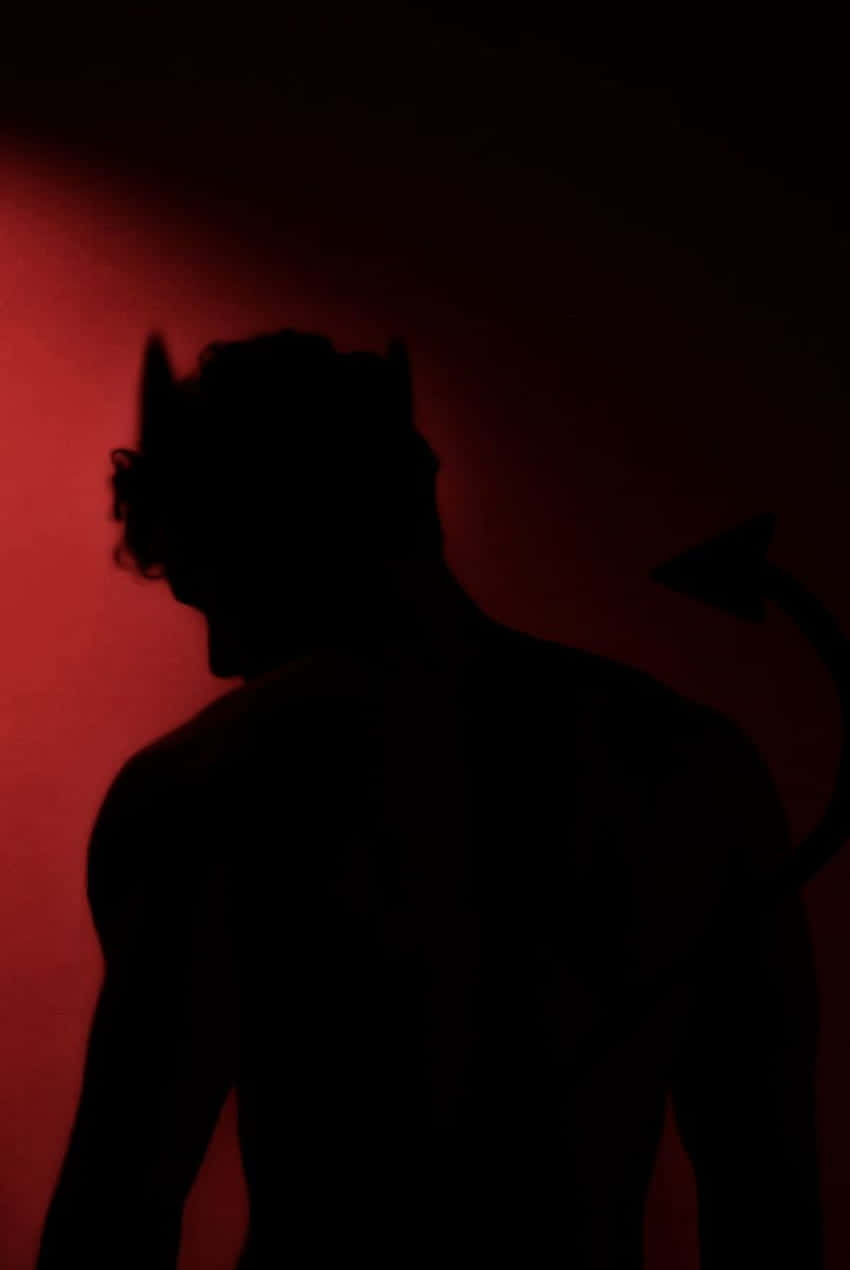  壁紙 — 在昏暗光線下，一個帶有角和尾巴的惡魔剪影映襯在發光的紅牆上。