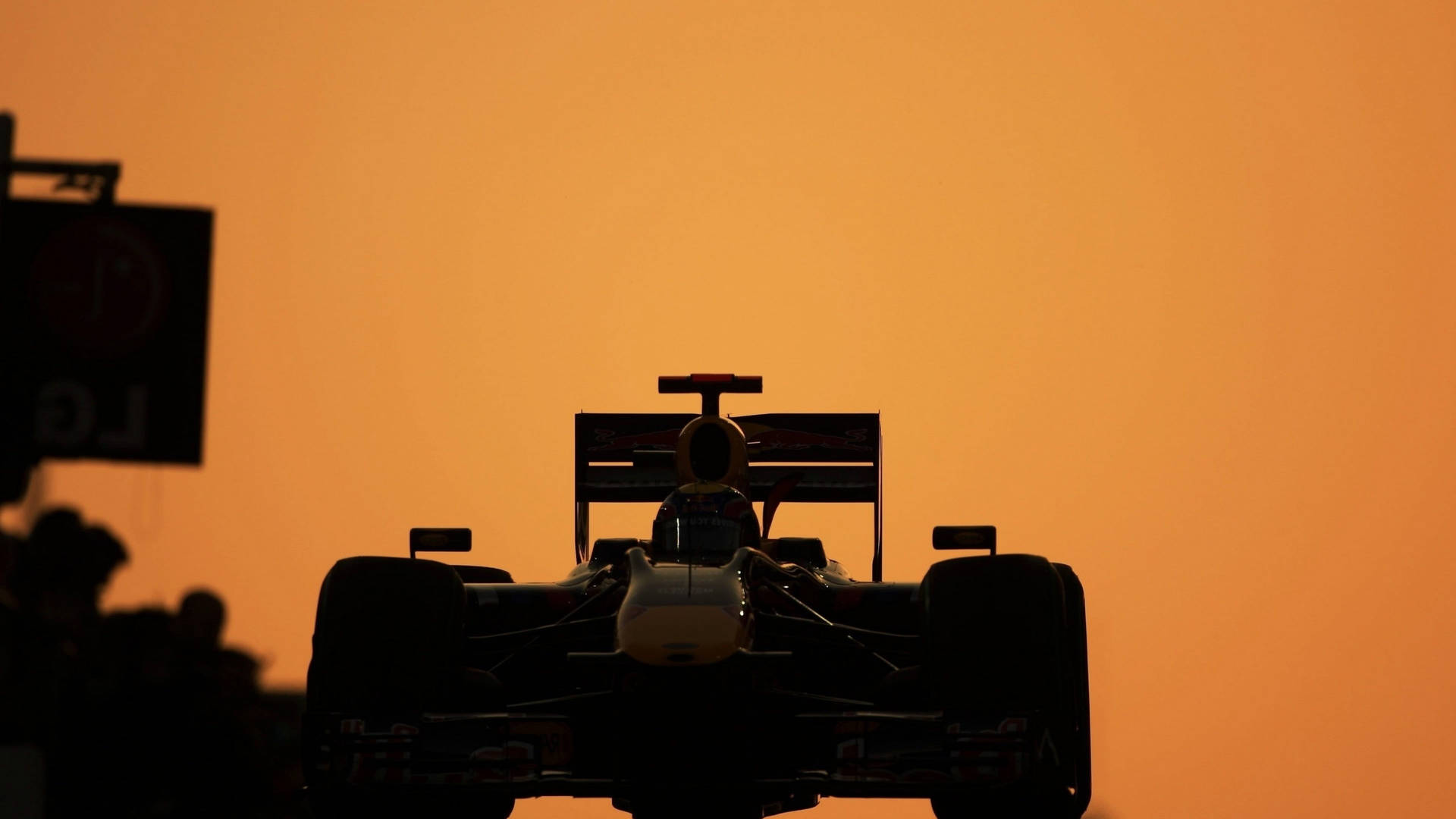 日落時分的賽車剪影，背景有觀眾 — F1 壁紙