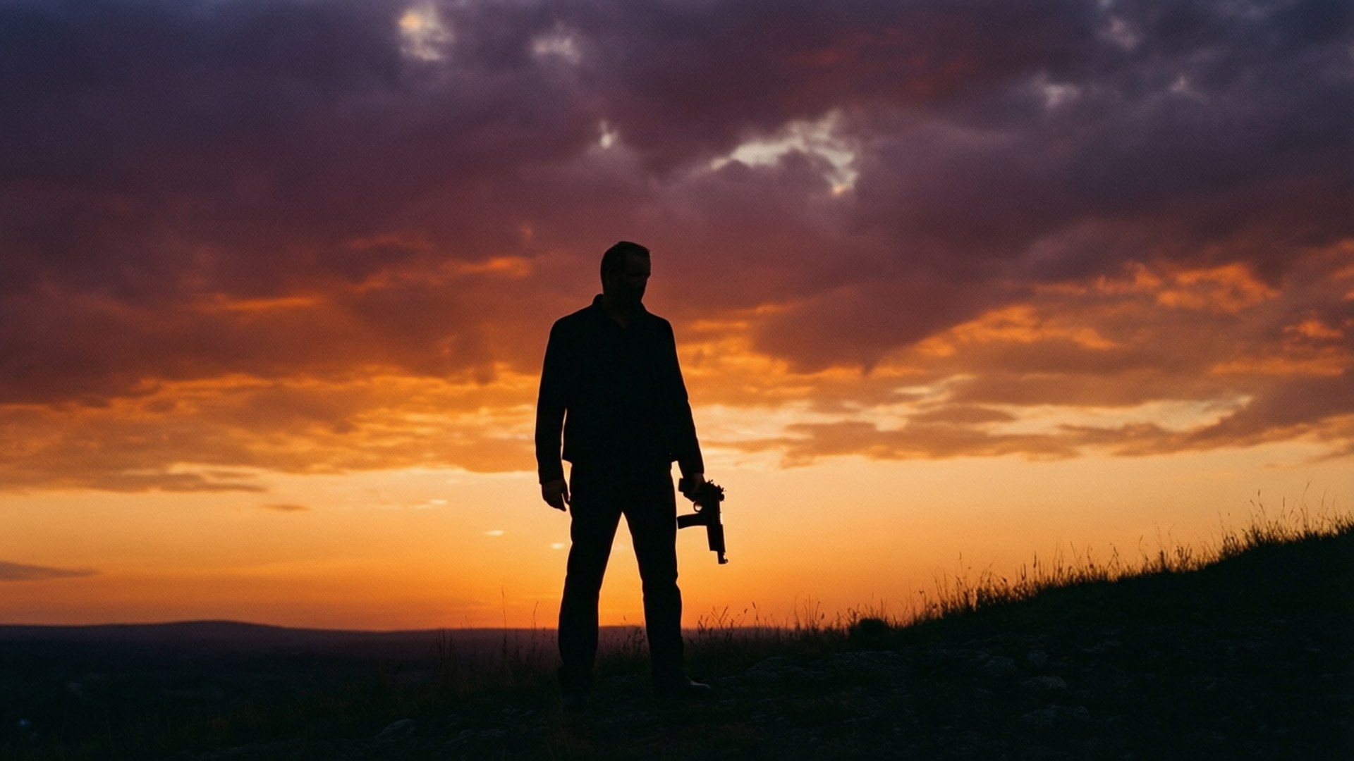 Gunman Silhouette Sunset 壁紙 — 一個孤獨的男人手持槍械的剪影，站在長滿草的山丘上，背景是火橙色和深紫色雲彩繪成的戲劇性日落天空。