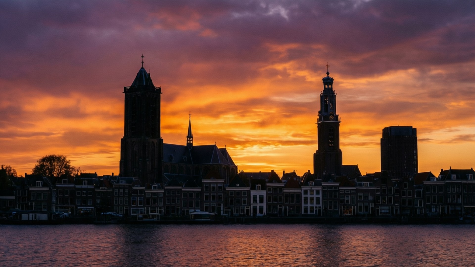 Amersfoort 桌布 壁紙 — 剪影般的歷史荷蘭建築和教堂塔樓，在平靜的水面倒映著火熱的橙色和紫色日落天空。
