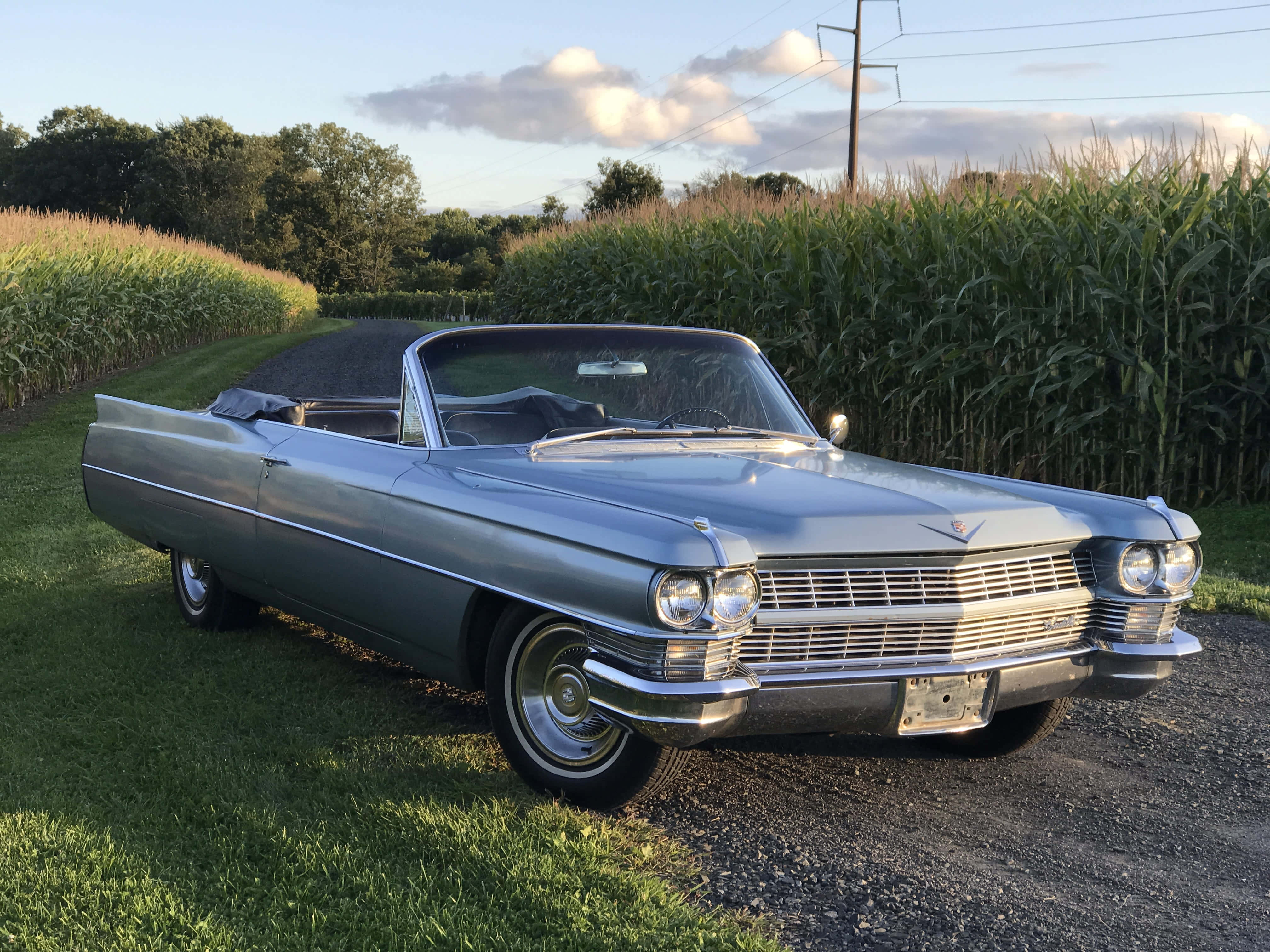 Cadillac Deville 桌布 壁紙 — 一輛銀色1960年代凱迪拉克敞篷車停泊在日落時分高聳玉米田旁的碎石路上。