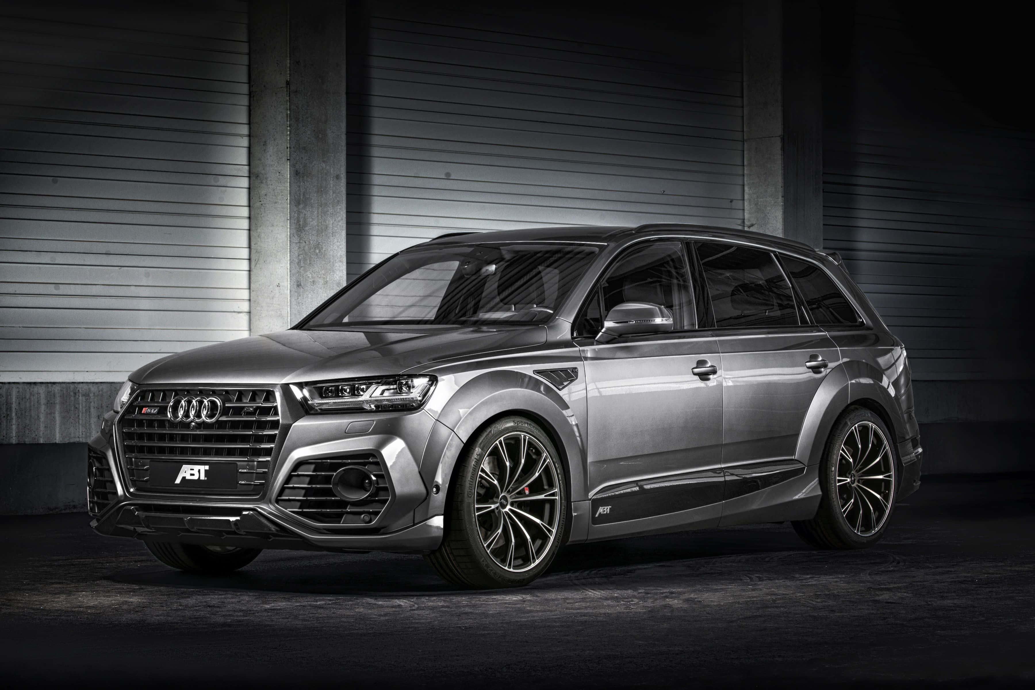 Audi Q7 桌布 壁紙 — 一輛時尚的銀色ABT Audi SQ8 SUV配黑色輪圈，停在光線昏暗的工業車庫中，車庫有混凝土牆和金屬壁板。