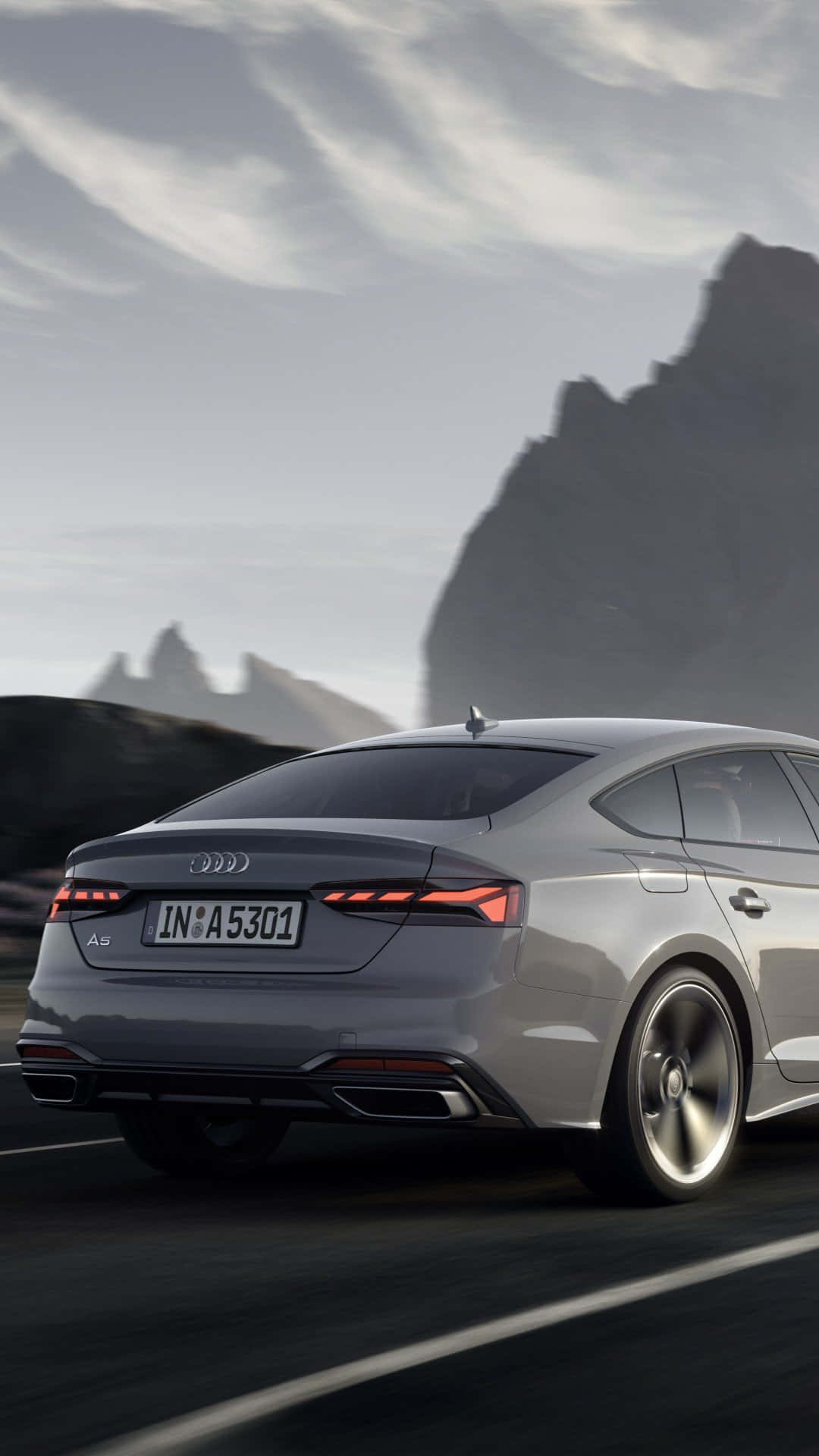 Audi A5 桌布 壁紙 — 一輛時尚的銀色奧迪A5轎車在蜿蜒的山路上行駛，天空多雲，背景是鋸齒狀的山峰。