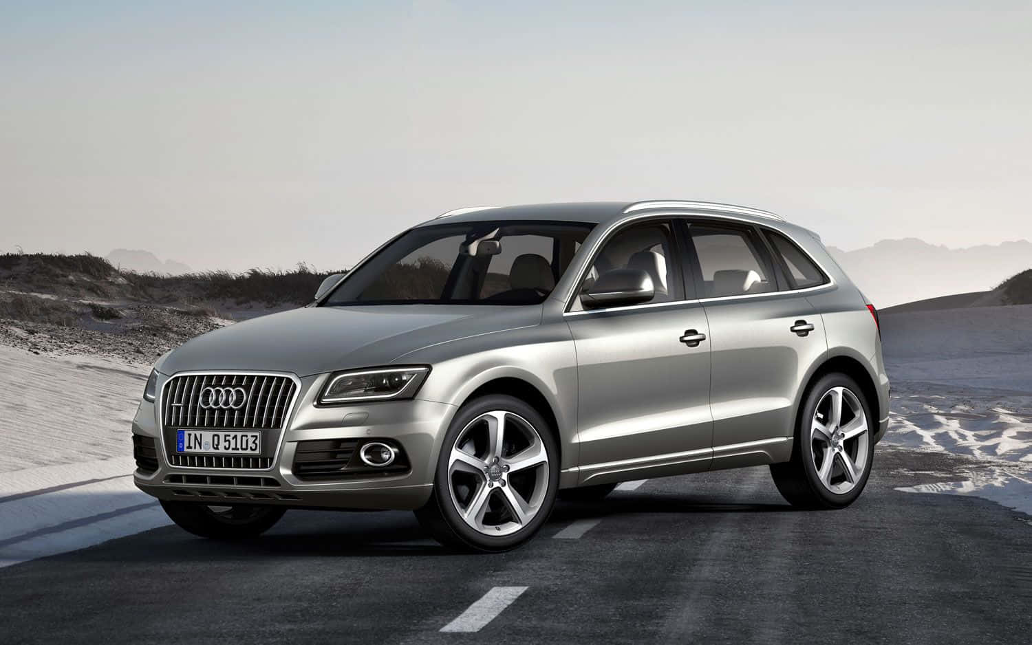 Audi Q5 桌布 壁紙 — 一輛時尚的銀色奧迪Q5 SUV在朦朧的天空下，行駛在穿越荒蕪沙漠景觀的柏油路上。