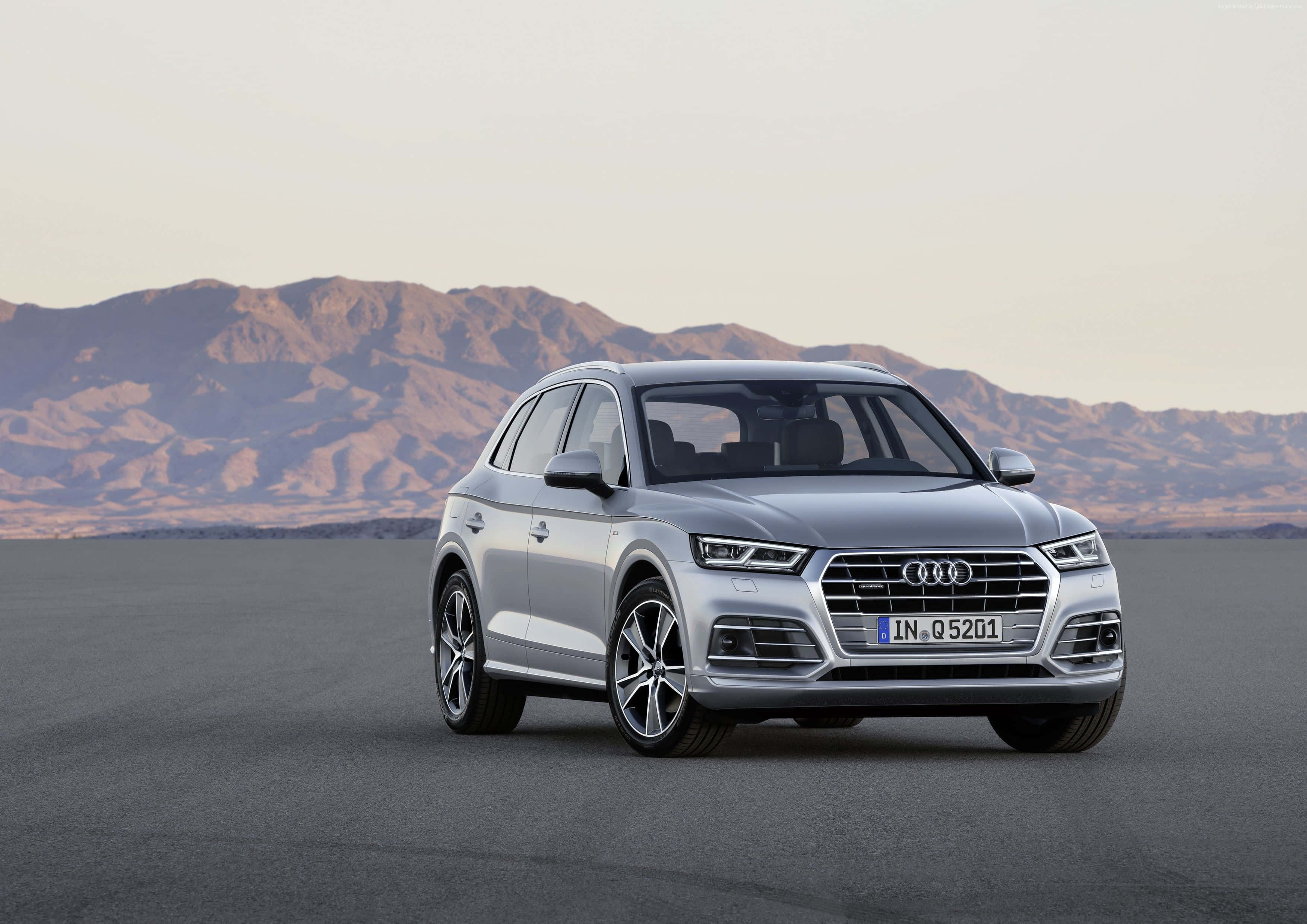 Audi Q5 桌布 壁紙 — 一輛時尚的銀色 Audi Q5 SUV 停泊在廣闊的沙漠平原上，遠山在朦朧的天空下若隱若現。