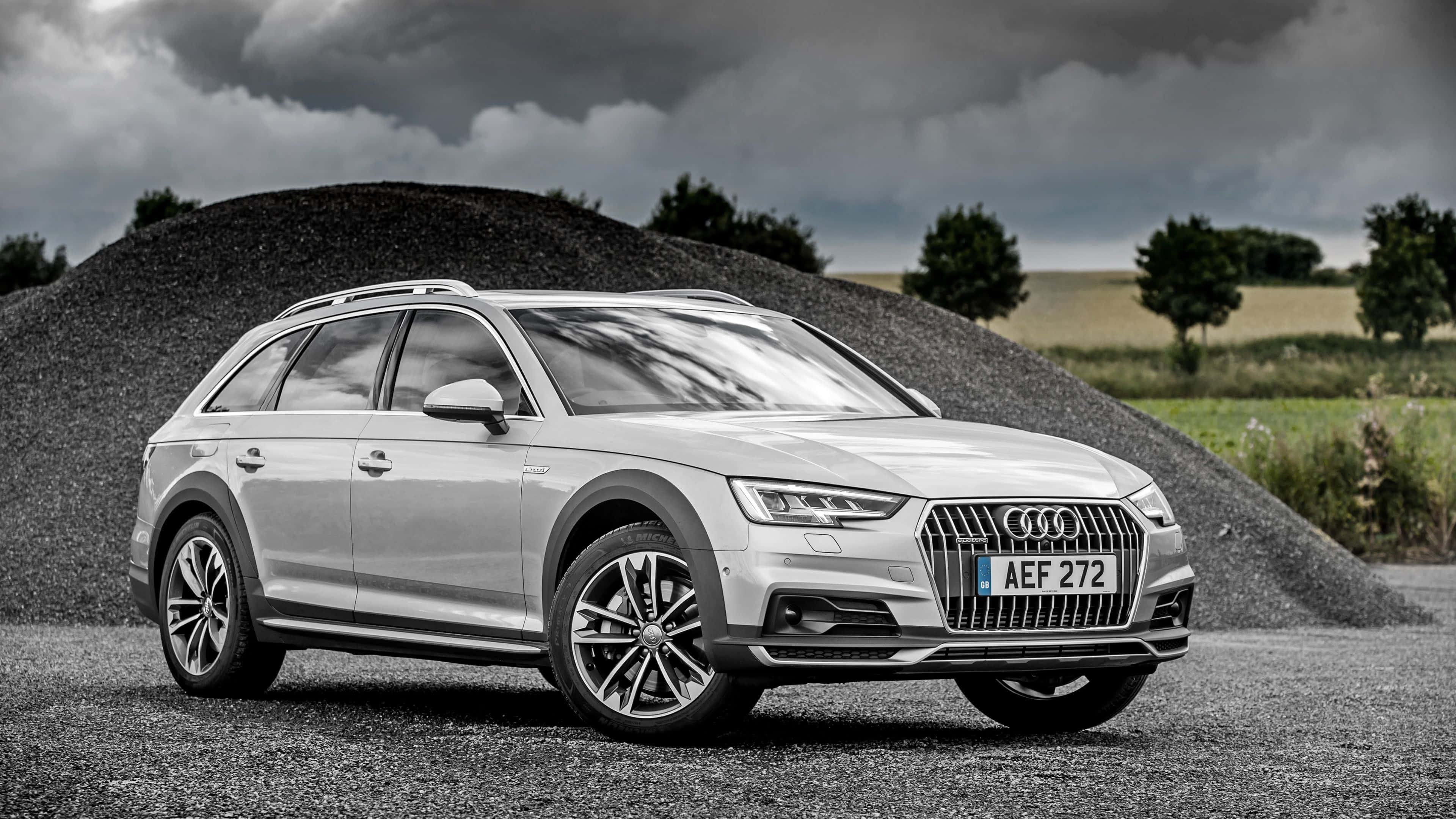 Audi A4 桌布 壁紙 — 一輛時尚的銀色 Audi 旅行車停泊在碎石上，旁邊是一大堆碎石，背景是戲劇性的多雲天空。