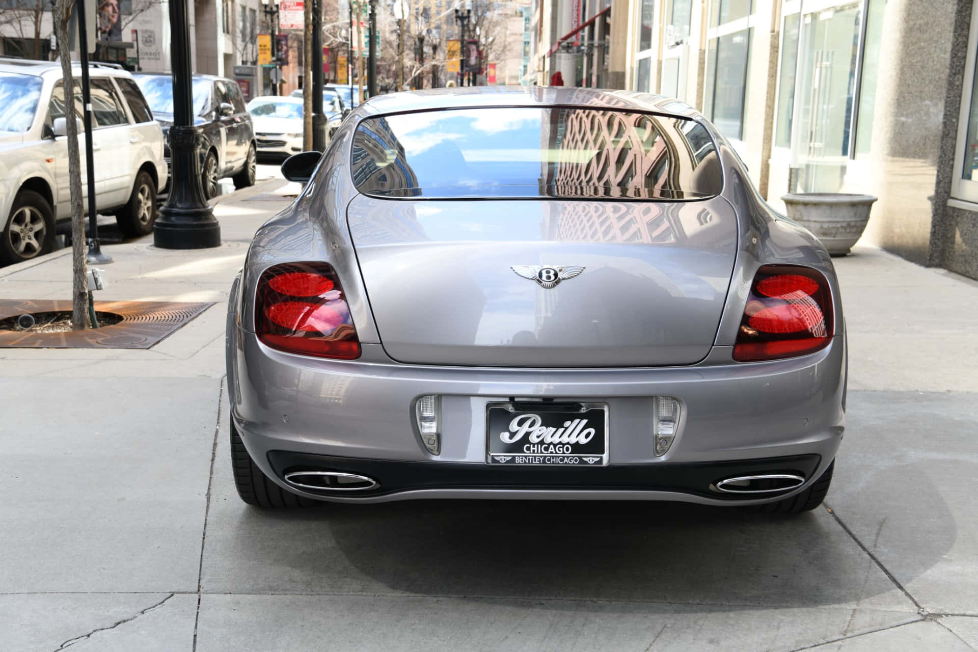 Bentley Continental Supersports 桌布 壁紙 — 一輛銀色賓利 Continental GT 停放在城市人行道上，其光亮的後窗反射出裝飾圍欄和城市建築。