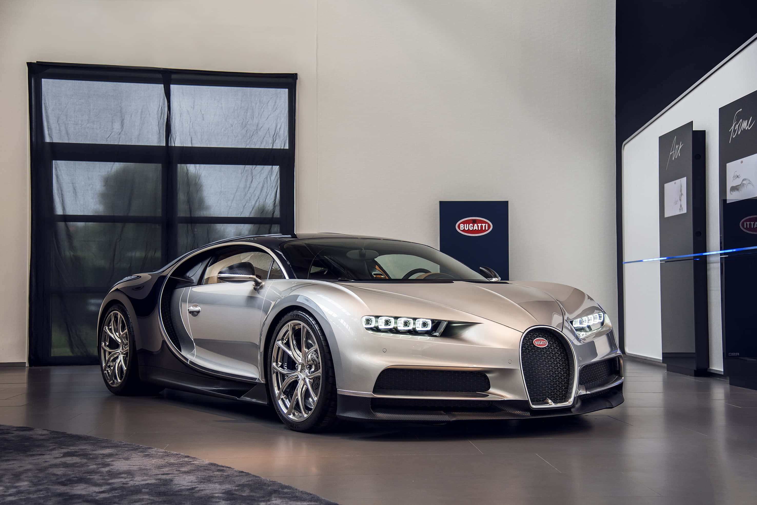 Bugatti Chiron 桌布 壁紙 — 一輛時尚的銀色Bugatti Chiron跑車在工作室燈光下閃耀，位於簡約豪華陳列室中，帶有黑色點綴和品牌展示。