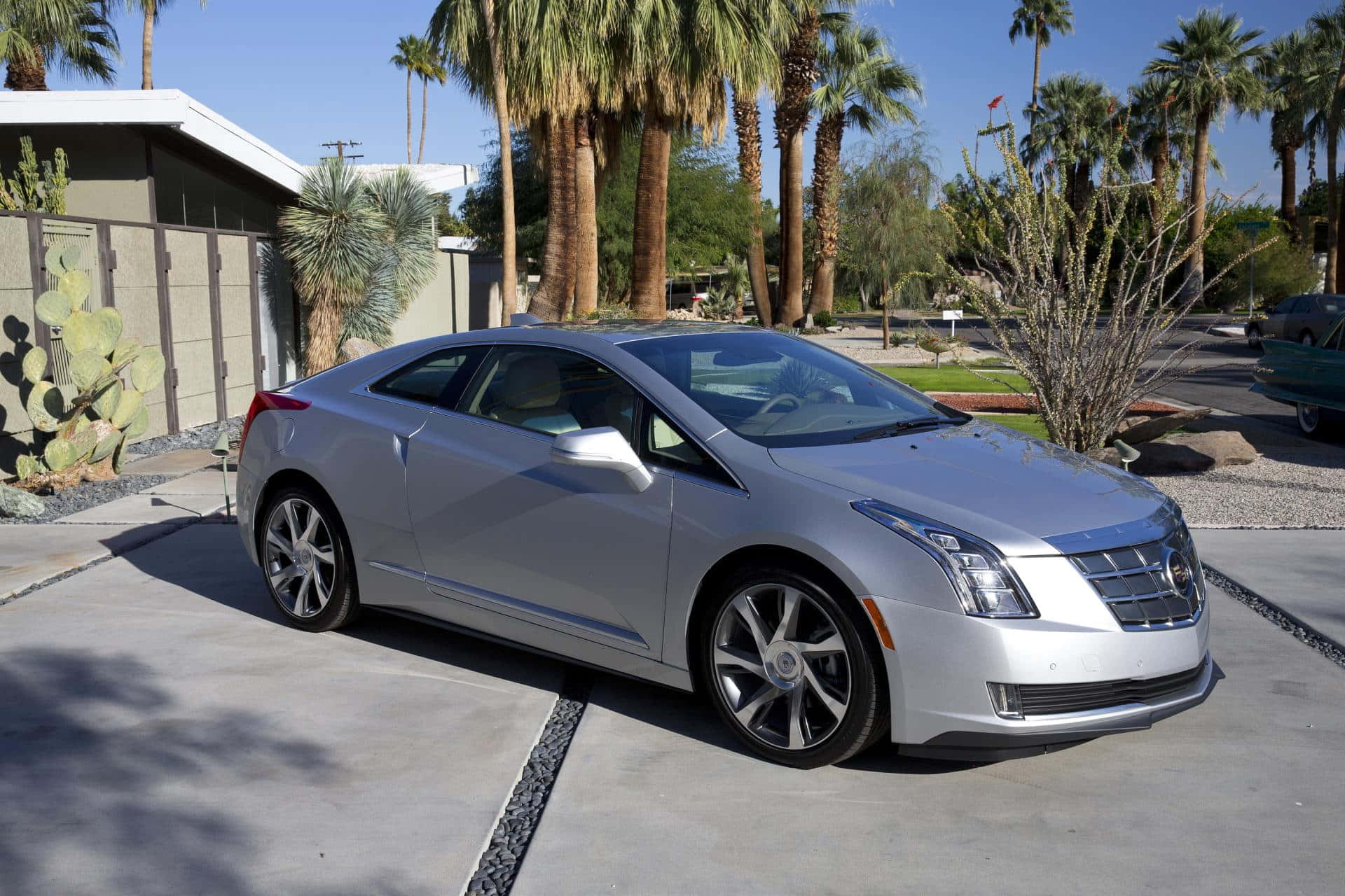 Cadillac Elr 桌布 壁紙 — 一輛時尚的銀色 Cadillac ELR 電動雙門轎跑車停在混凝土車道上，背景是明亮的沙漠陽光、棕櫚樹和仙人掌。