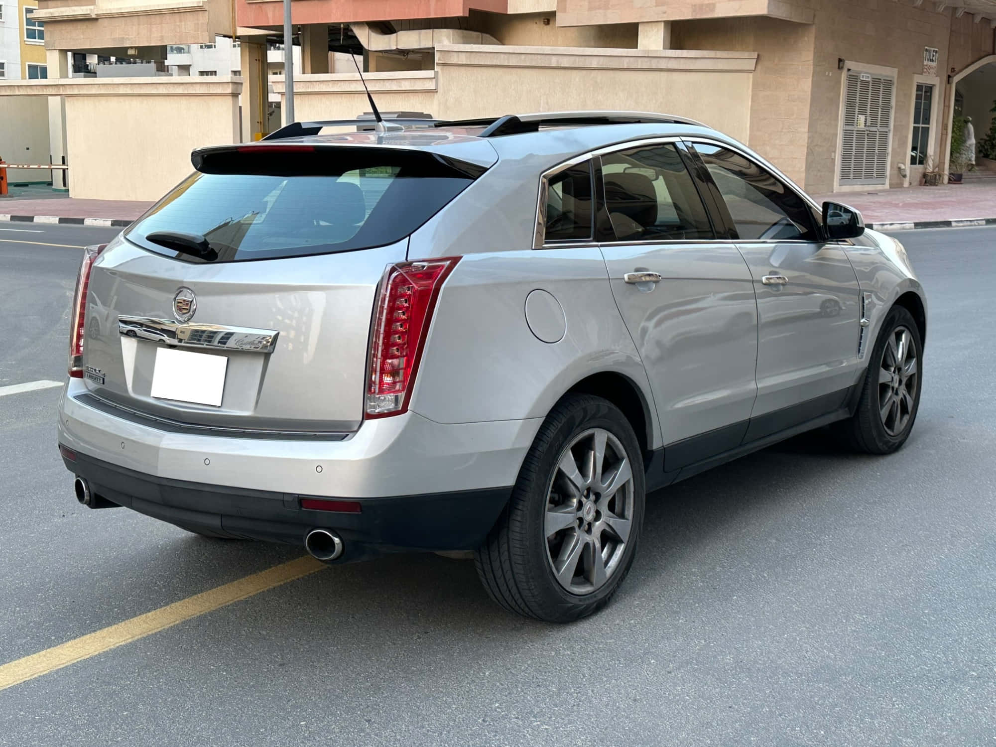 Cadillac Srx 桌布 壁紙 — 一輛銀色Cadillac SRX SUV停放在鋪砌的街道上，背景有建築物，在明亮的日光下。